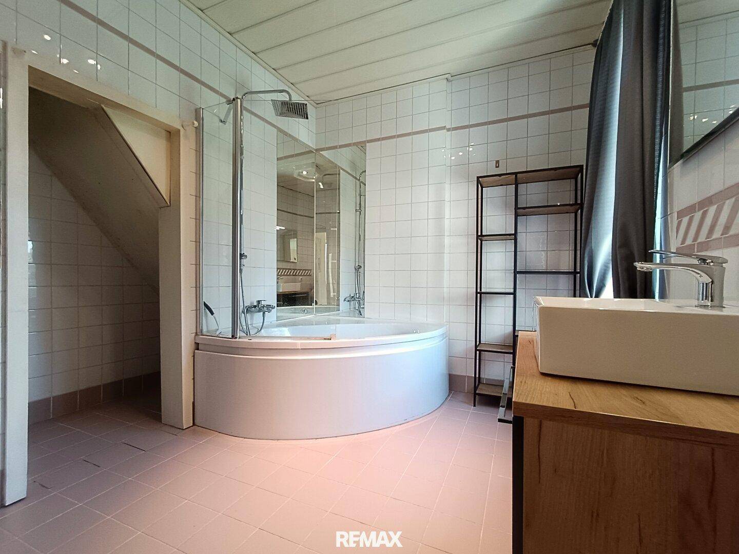 Badezimmer mit Eckbadewanne, Dusche und hellen Fliesen an Wänden und Boden.