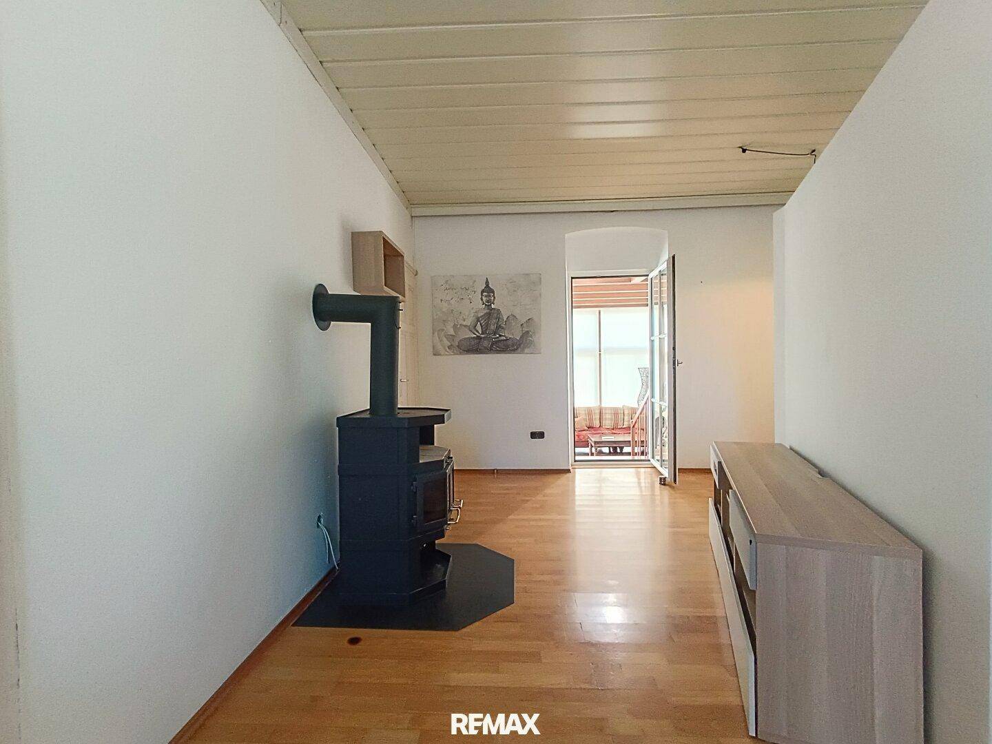 Wohnzimmer mit Holzboden, Kaminofen und Zugang zu einem Balkon oder Wintergarten.