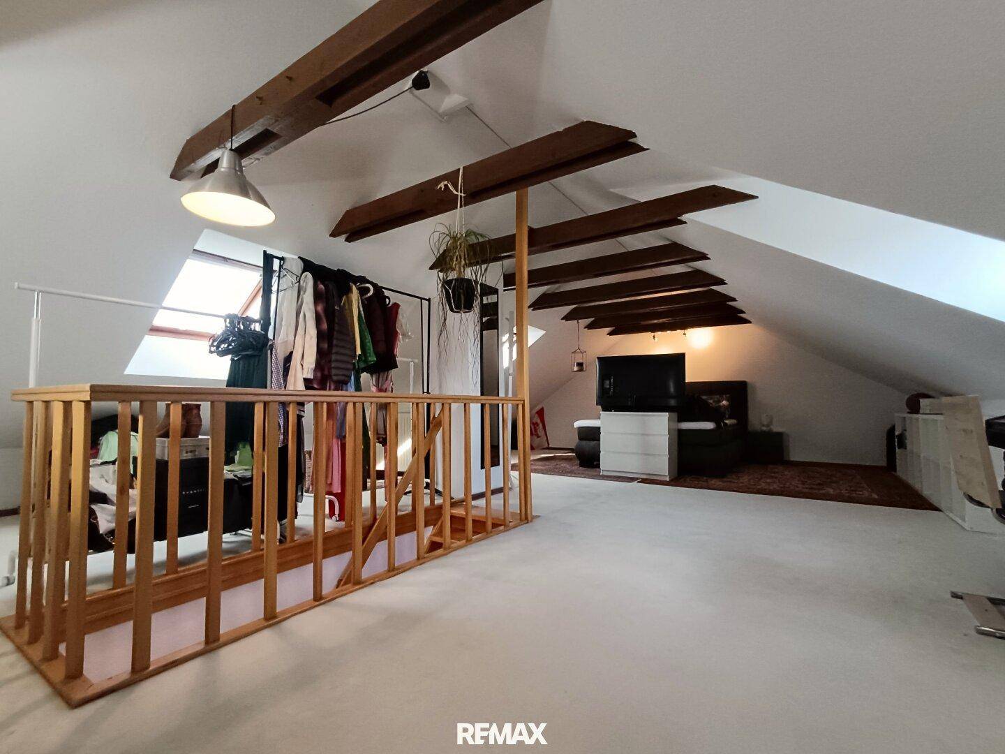 Ausgebauter Dachboden mit Holzbalken, Schrägen und offenem Schlafbereich.