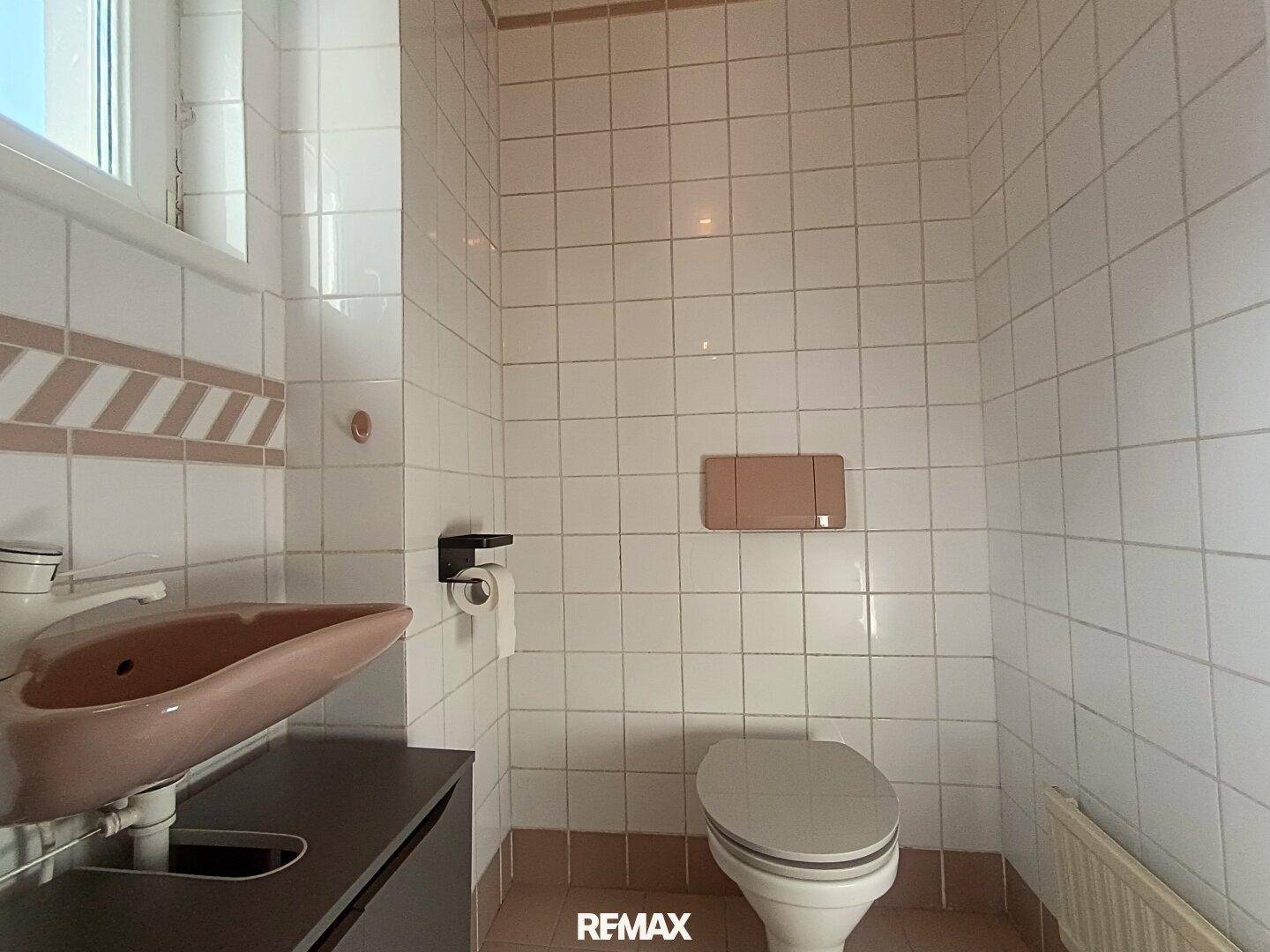 Kleines Badezimmer mit WC, Waschbecken und hellen Fliesen im Retro-Stil.
