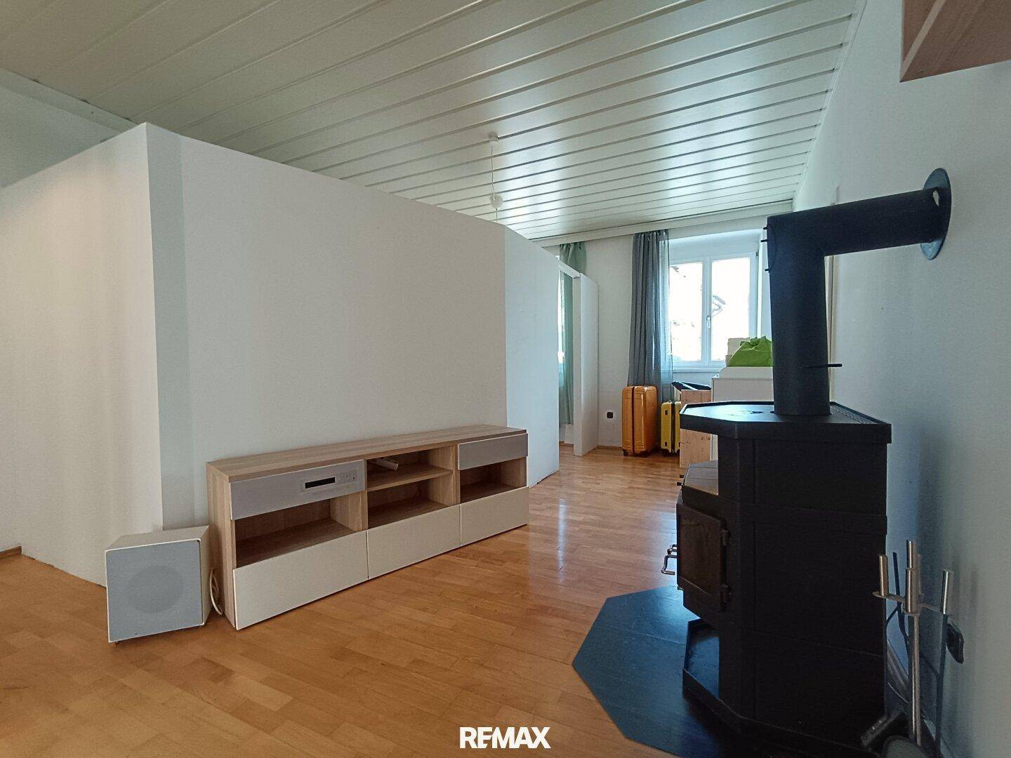 Geräumiges Wohnzimmer mit Kaminofen, Holzboden und Blick auf Fenster.