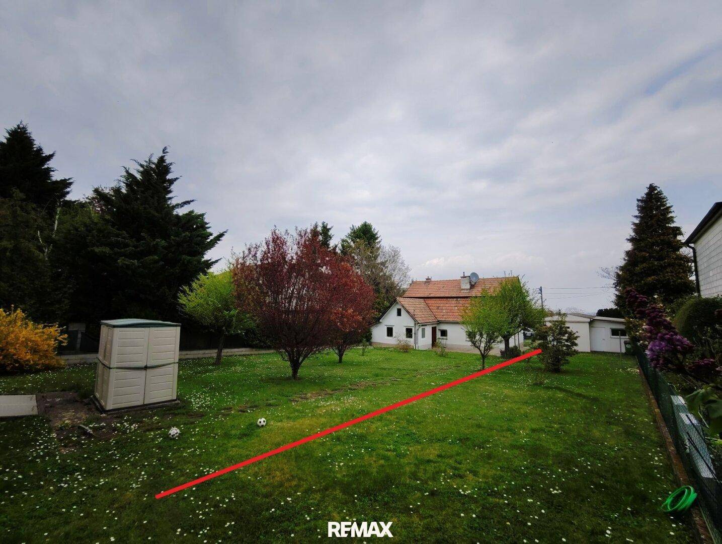 Grüner Gartenbereich mit Rasen, Bäumen und einem kleinen Geräteschuppen im Hintergrund.