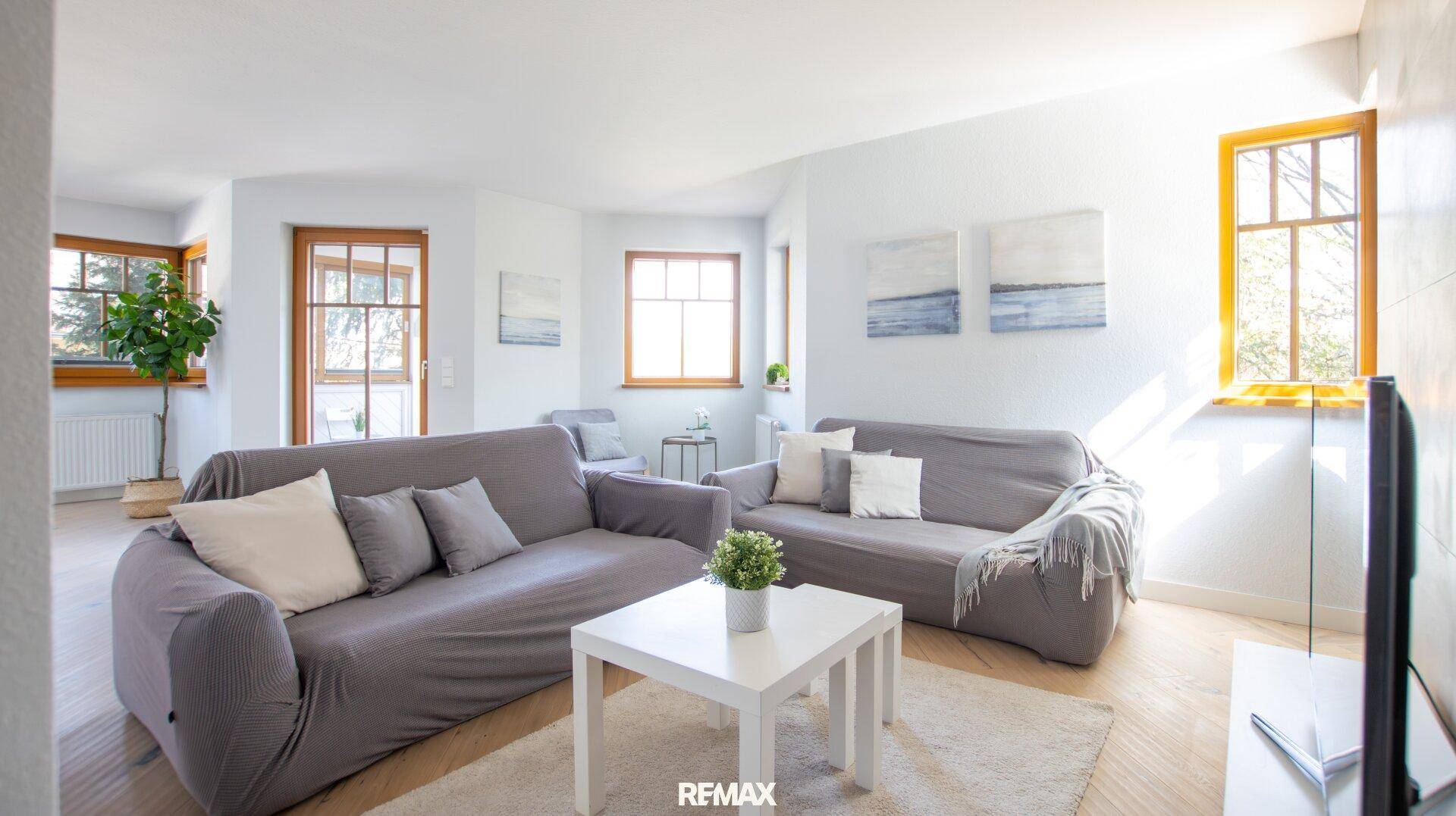 Gemütliches Wohnzimmer mit zwei grauen Sofas, Couchtisch und viel Tageslicht durch die Fenster.