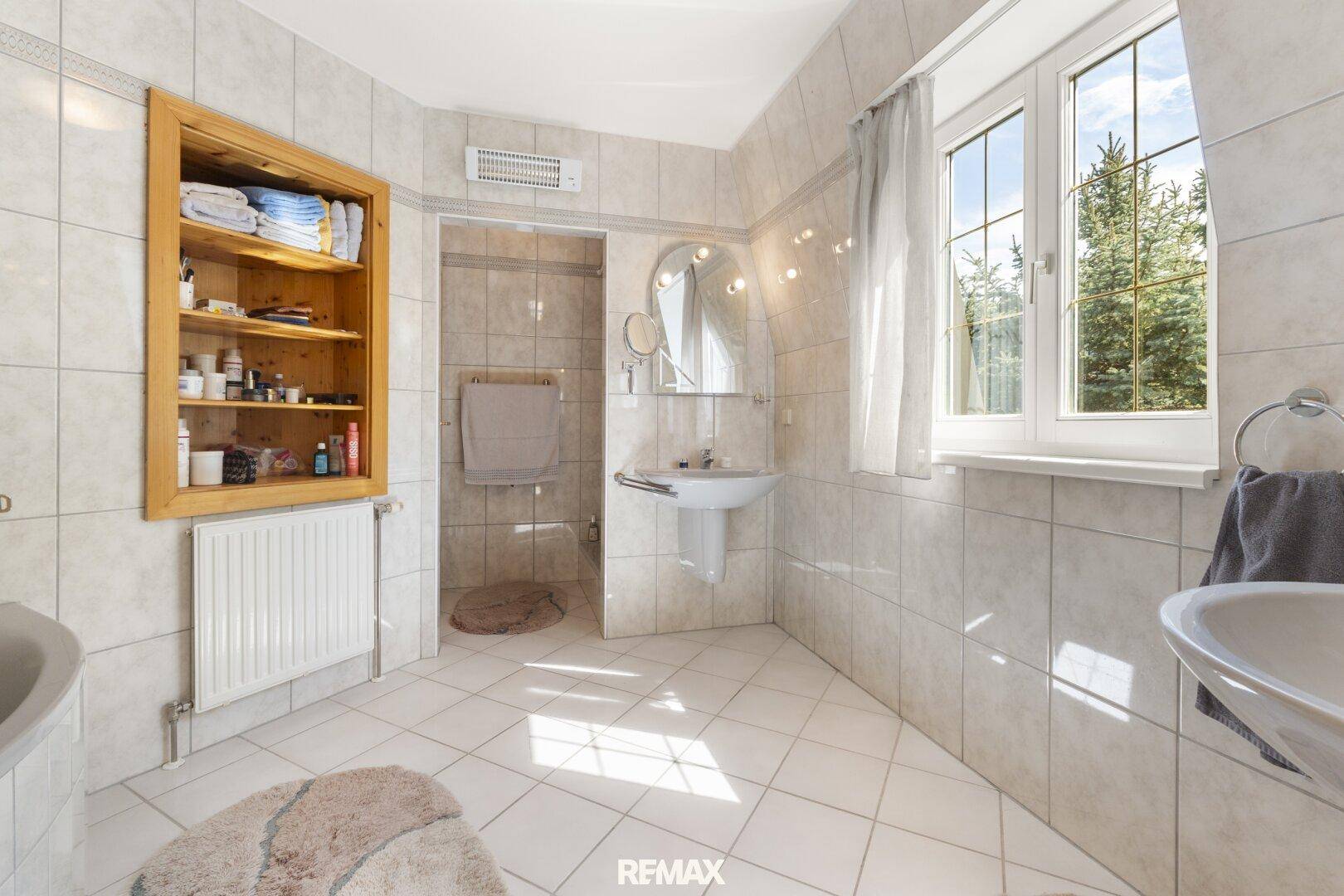 Gefliestes Badezimmer mit Dusche, Einzelwaschbecken und Fenster.