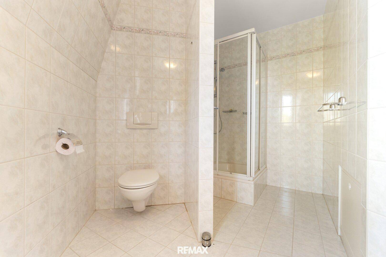 Kleines Badezimmer mit WC, Duschkabine und Fliesenboden.