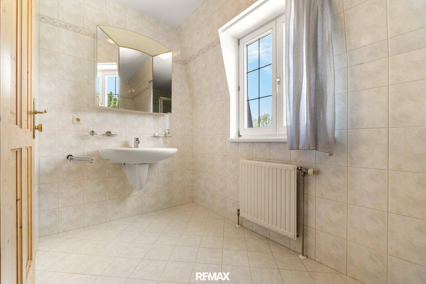 Helles Badezimmer mit Waschbecken, Spiegel und Fenster.