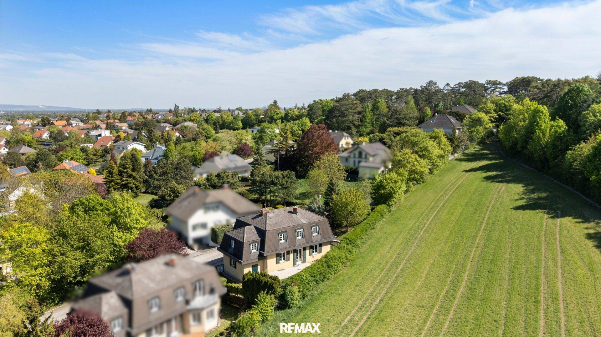 Malerische Luftaufnahme eines Hauses mit Mansarddach, umgeben von viel Grün und Feldern.