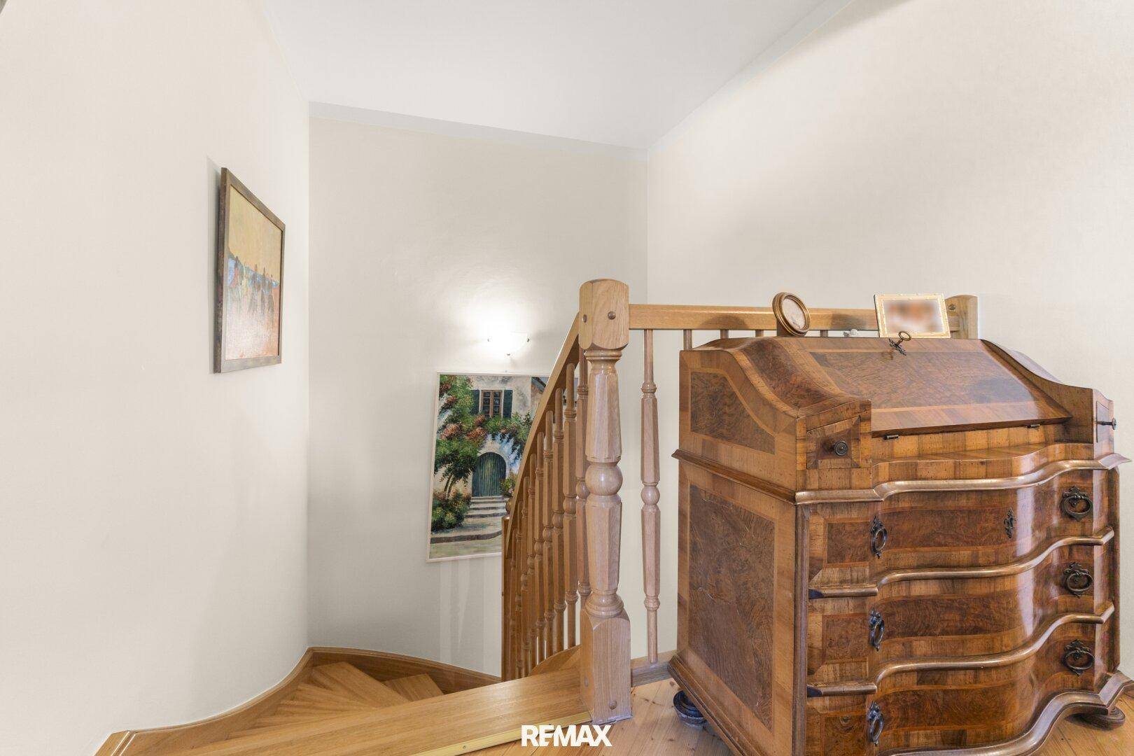 Elegantes Treppenhaus mit Holzgeländer und einem antiken Sekretär, der den Flur schmückt.