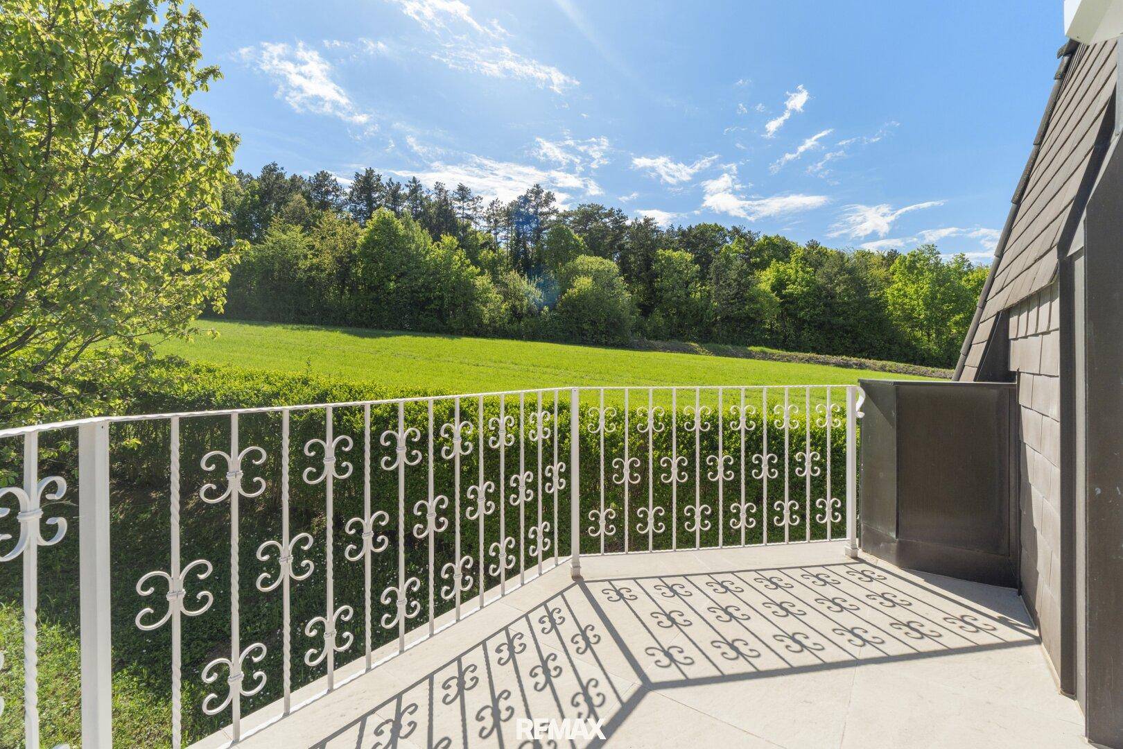 Sonniger Balkon mit schmiedeeisernem Geländer und weitem Blick ins Grüne.