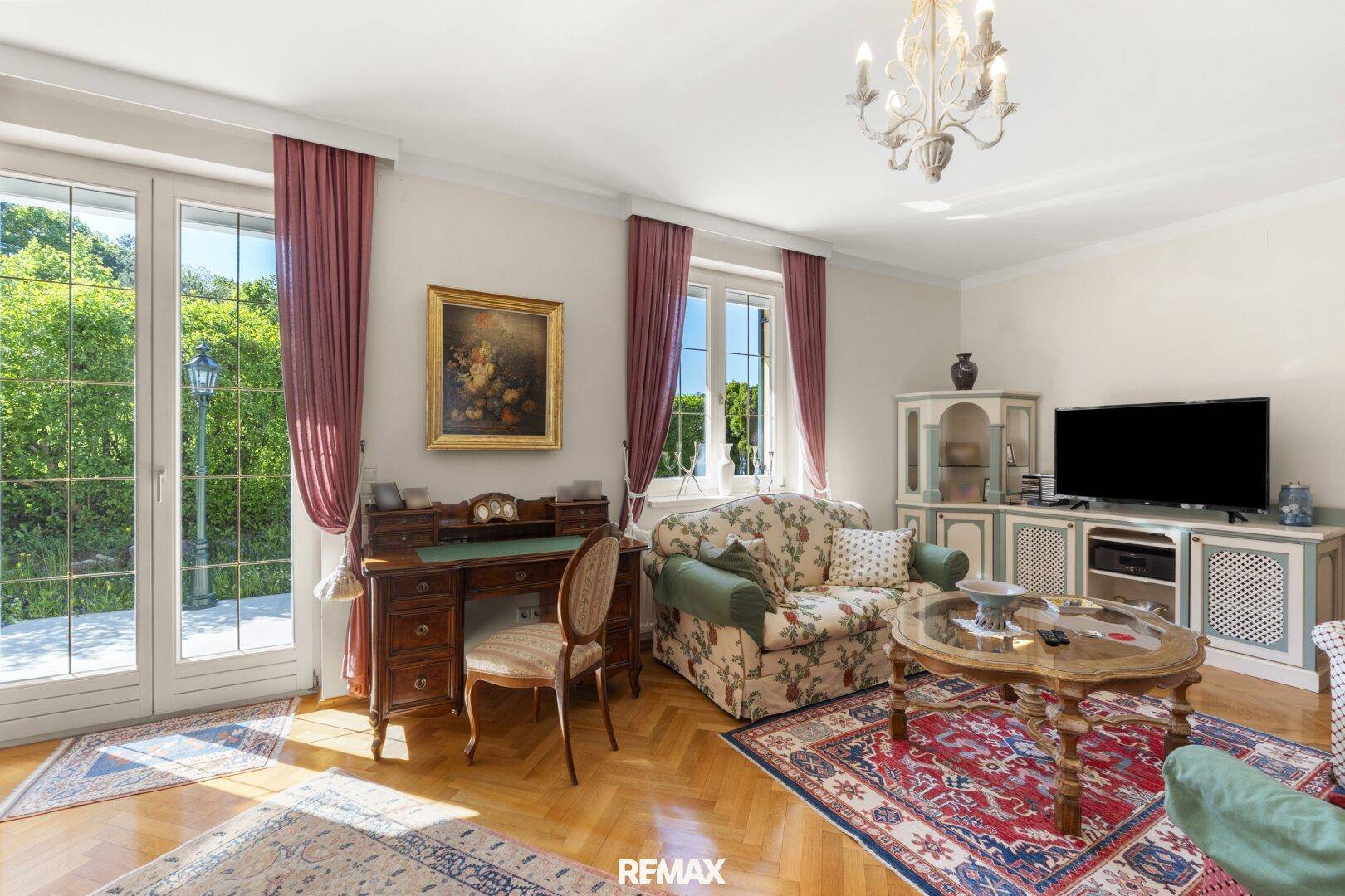Helles Wohnzimmer mit traditionellen Möbeln, Parkettboden und Zugang zu einem grünen Außenbereich.