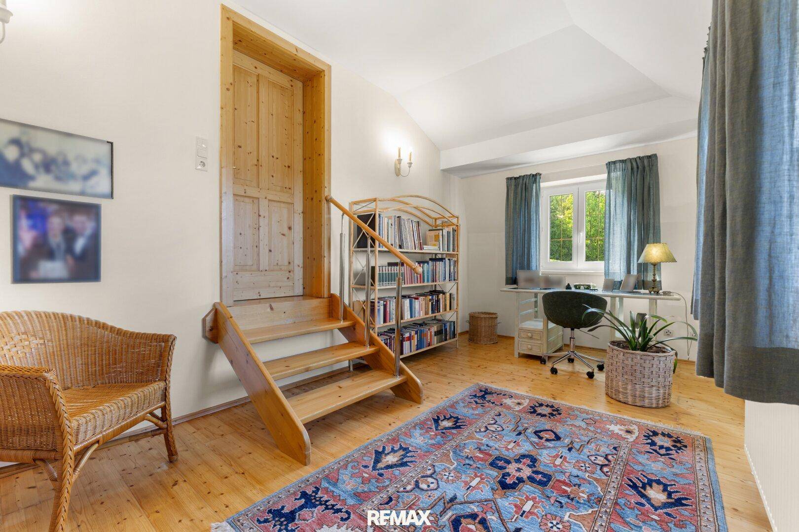 Vielseitiges Zimmer mit Holzboden, Bücherregal und Zugang zu einem weiteren Bereich über eine Holztreppe.