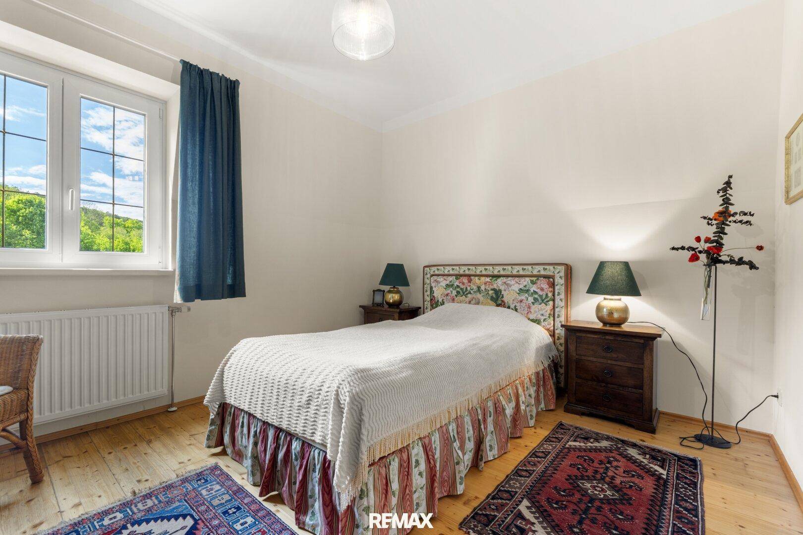 Gemütliches Schlafzimmer mit Einzelbett, Holzboden und einem Fenster, das einen schönen Blick ins Grüne bietet.