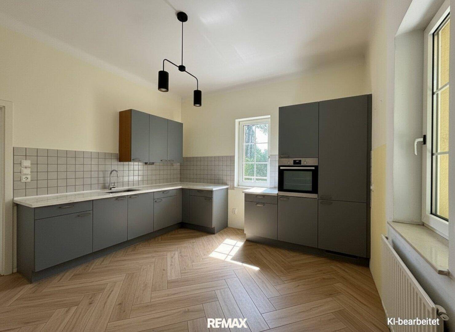 Moderne Küche mit grauen Schränken, Holzparkett und Fensterblick ins Grüne.