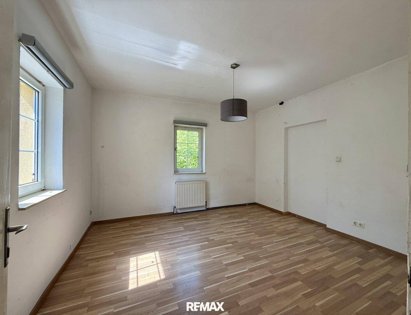 Leeres Zimmer mit Holzboden, Fenster und Heizkörper, bereit zur individuellen Gestaltung.