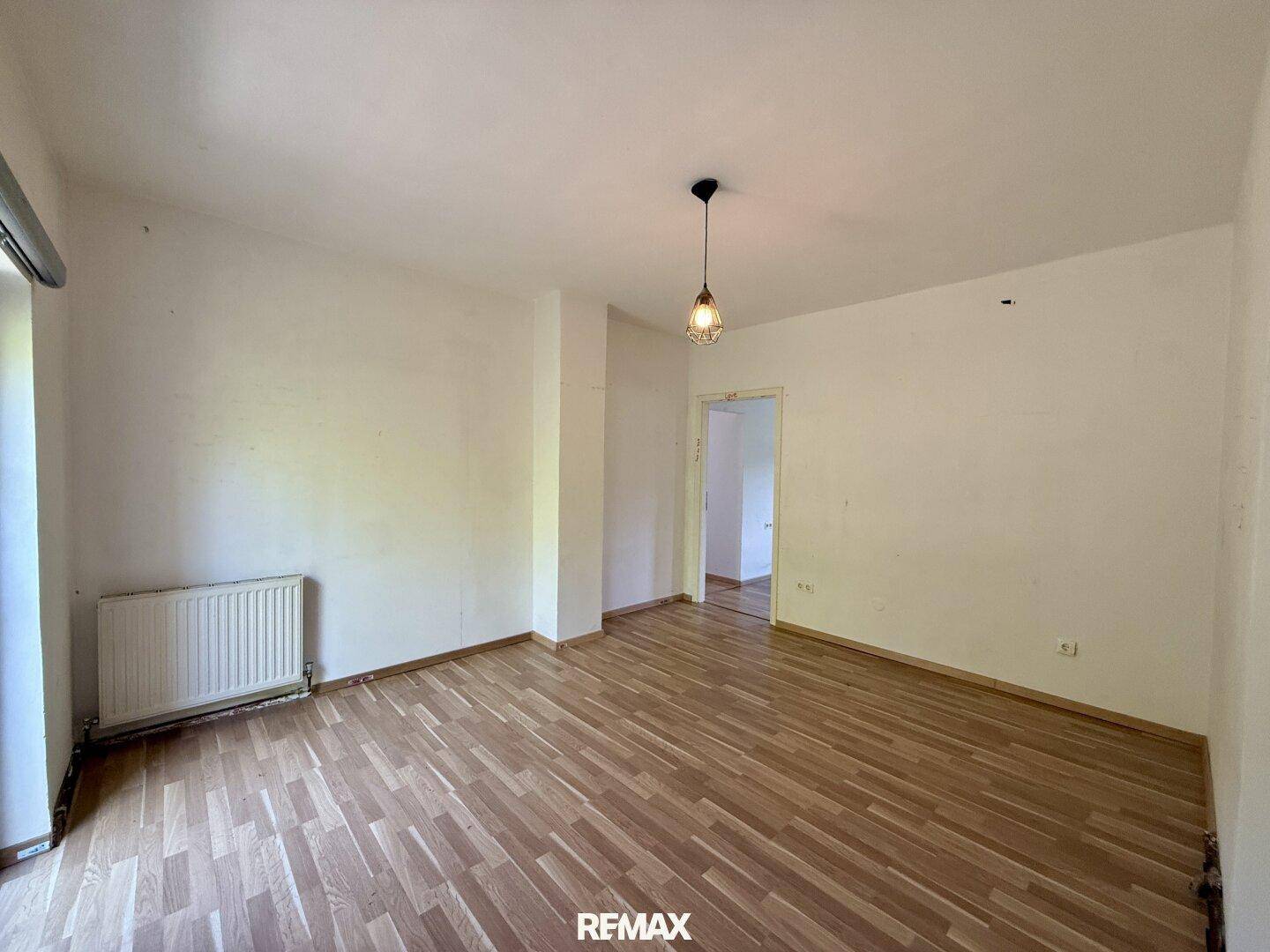 Leeres Zimmer mit Parkettboden und Heizkörper unter einem Fenster.