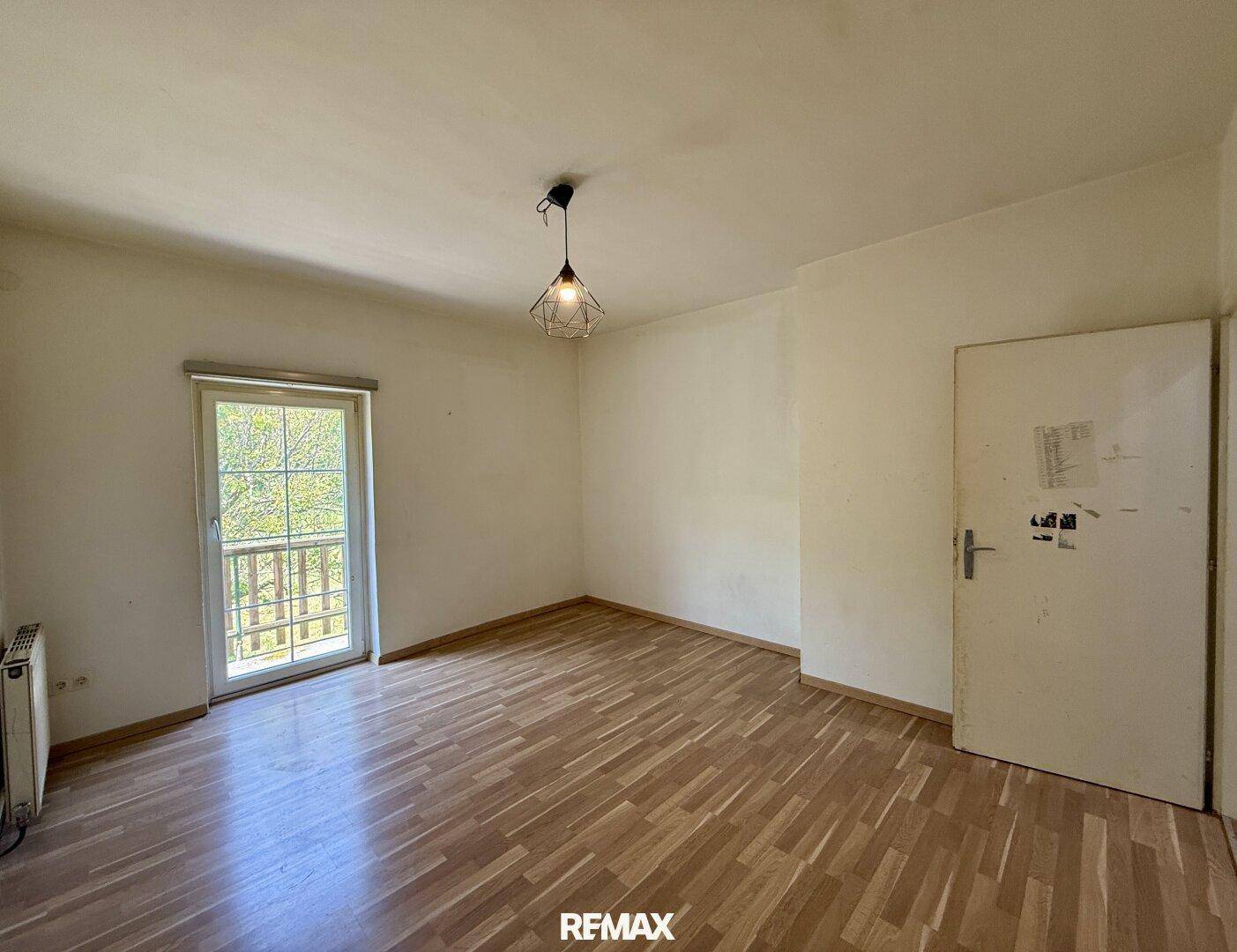 Leeres Zimmer mit Parkettboden und Zugang zu einem französischen Balkon.