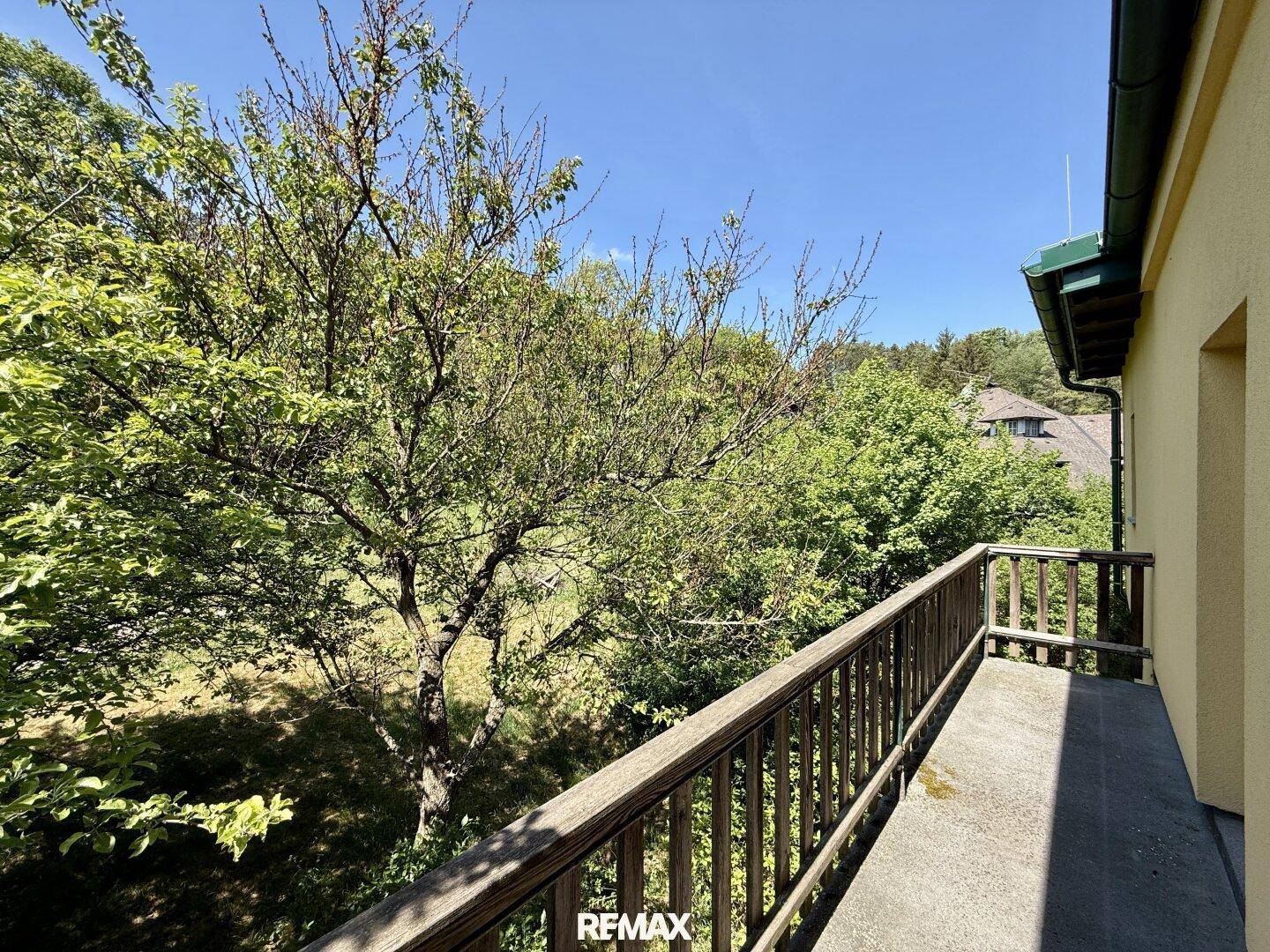 Balkon mit Holzgeländer und Blick auf den grünen Garten und alte Bäume.