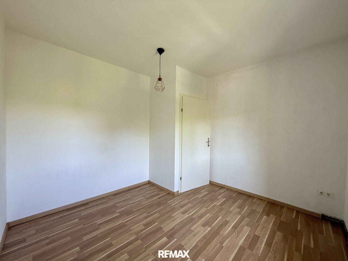 Leeres Zimmer mit Parkettboden und einer geschlossenen Tür.