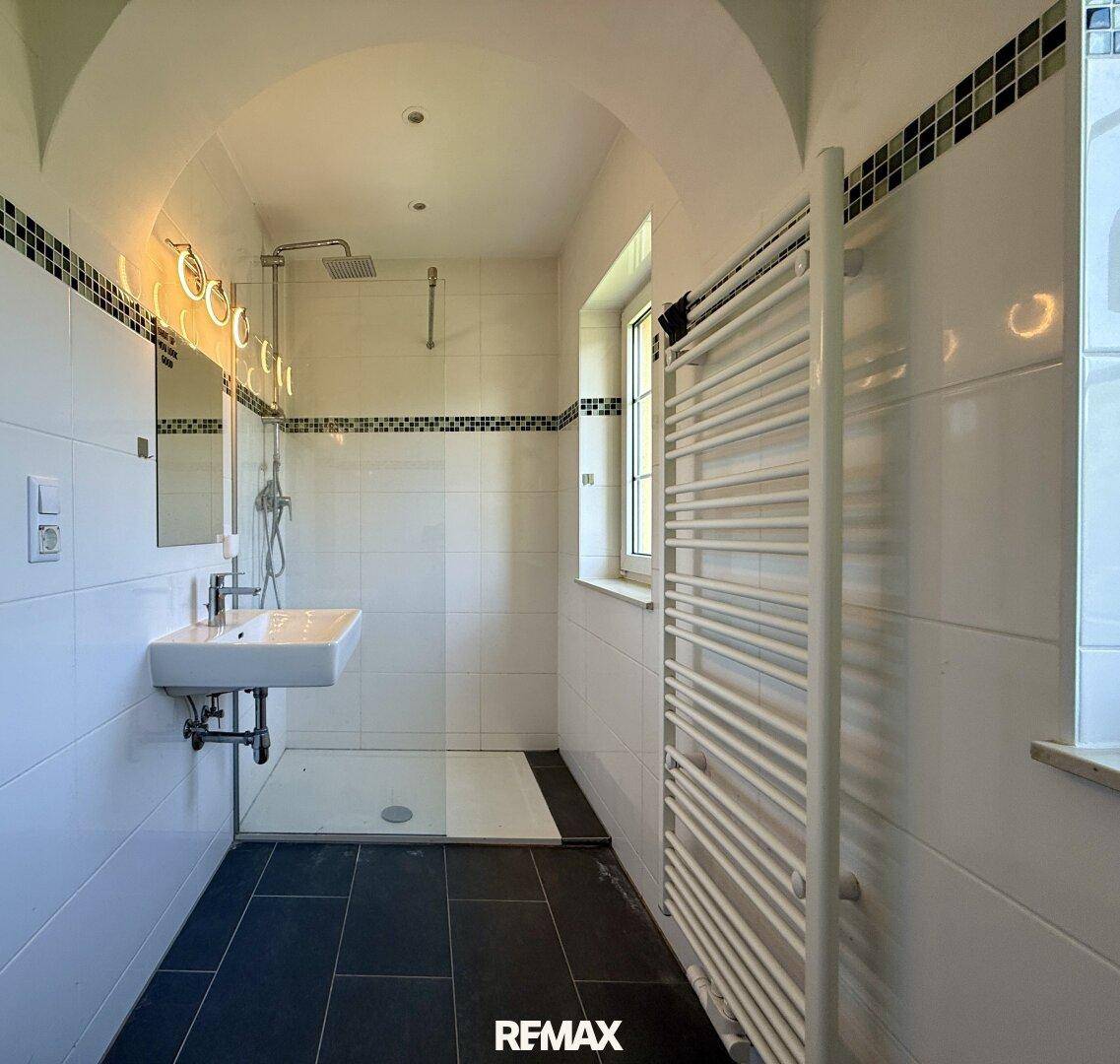 Modernes Badezimmer mit begehbarer Dusche, weißen Fliesen und Handtuchheizkörper.