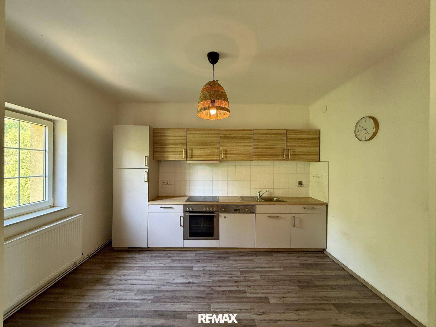 Kleine Küche mit weißen und holzfarbenen Schränken, Kühlschrank und Kochfeld.