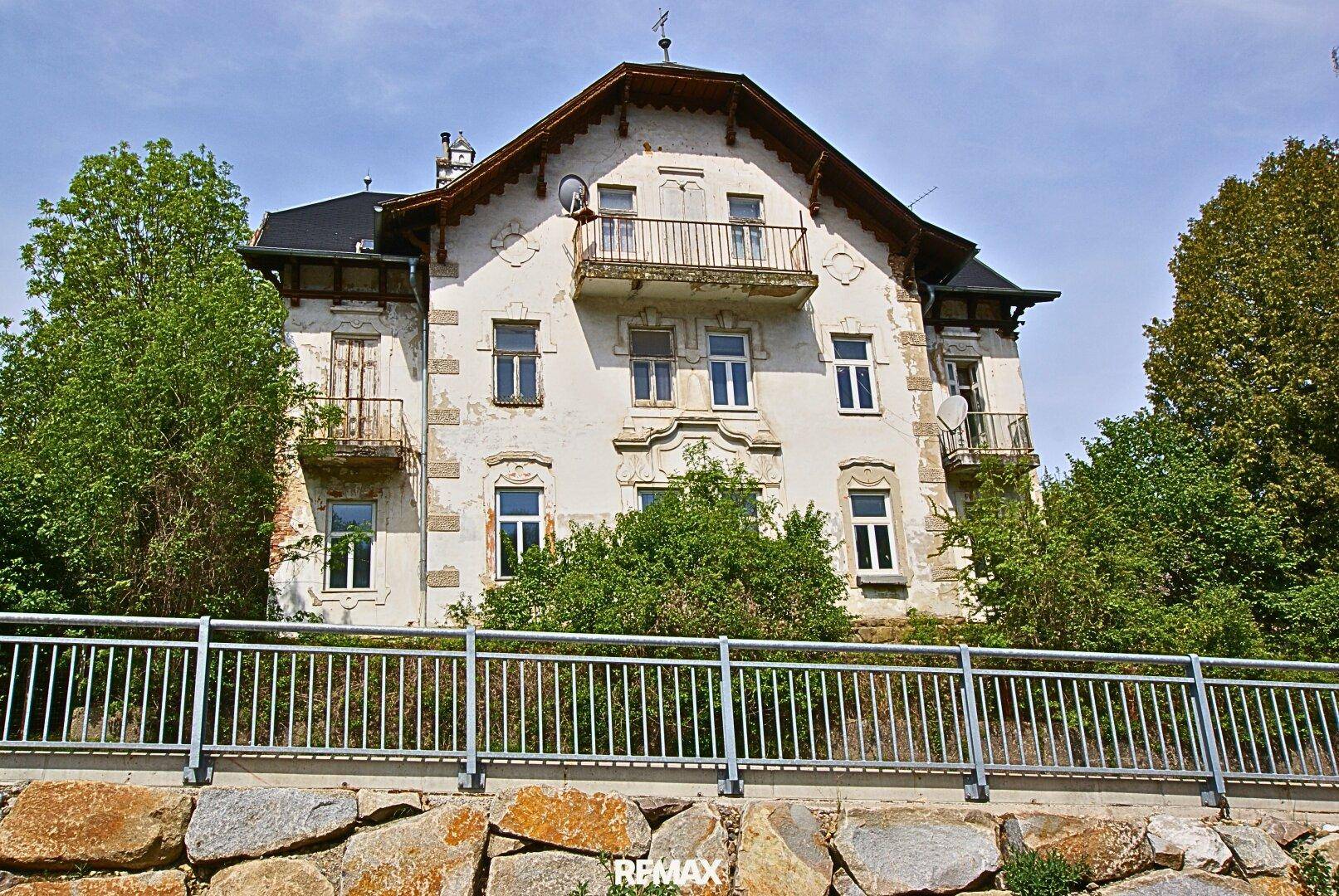 Historische Fassade eines Altbaus mit Balkonen und dekorativen Elementen, umgeben von Bäumen.