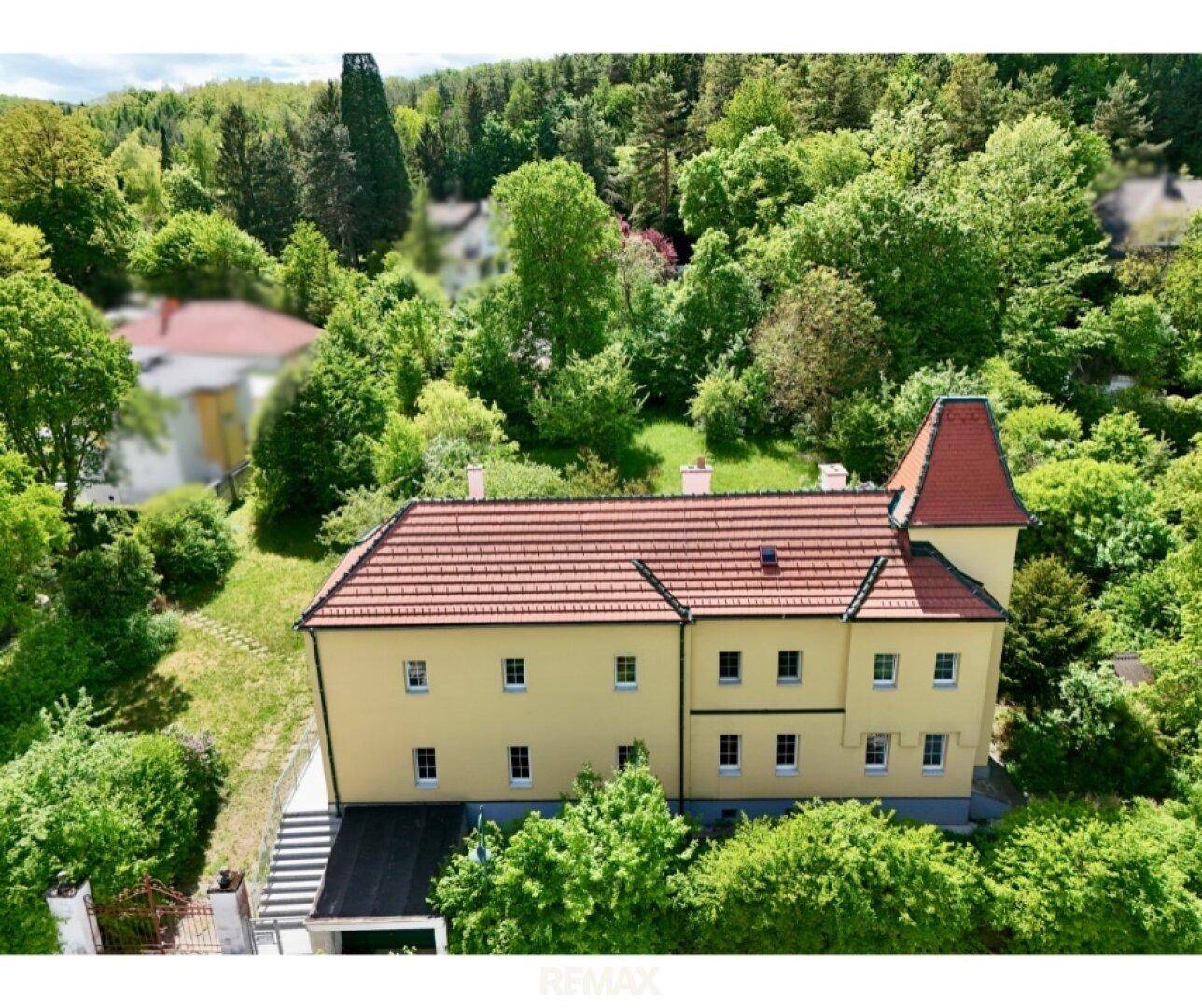 Luftaufnahme des gelben Gebäudes von einer anderen Seite, umgeben von üppigem Grün.