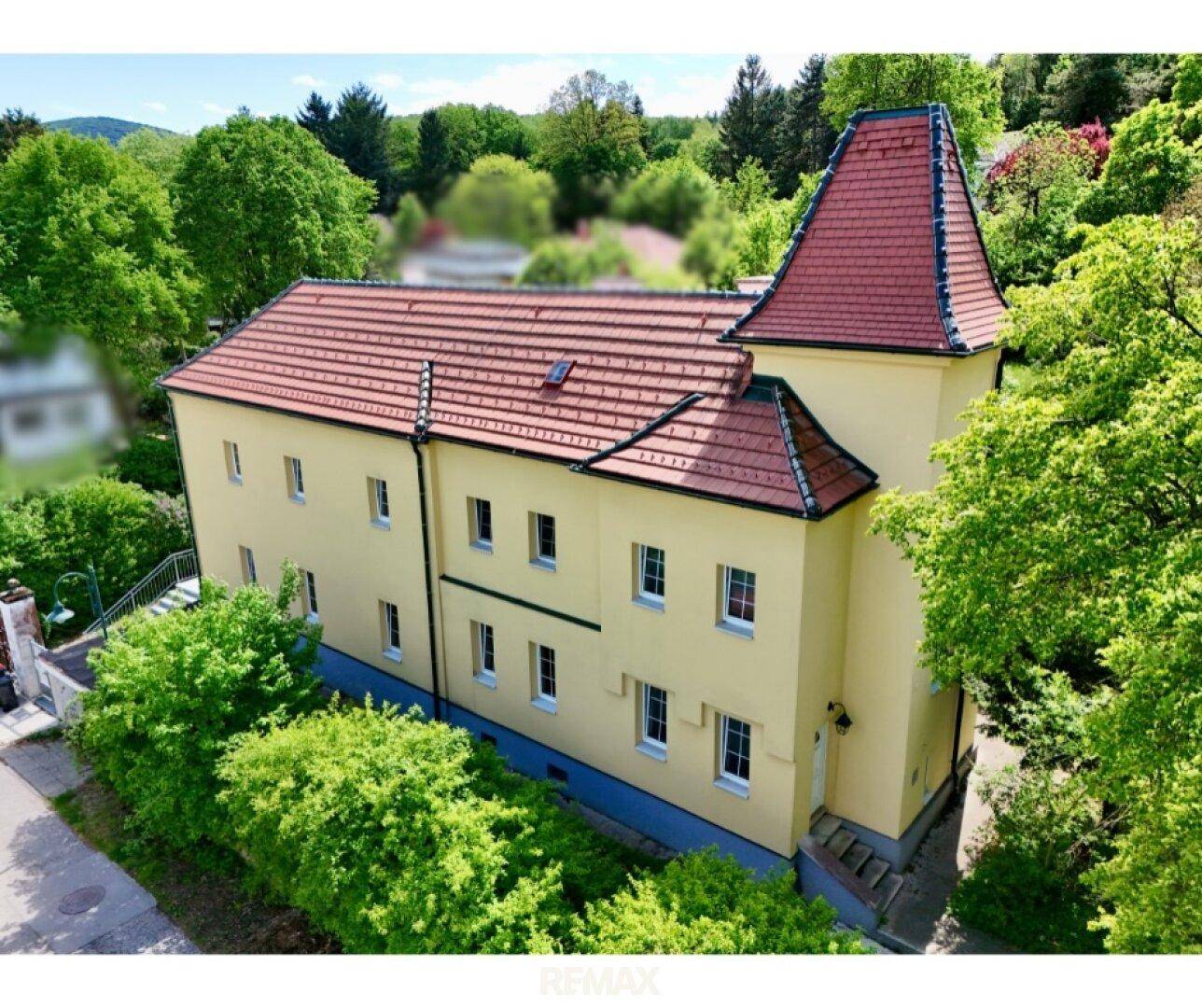 Historisches Gebäude mit gelber Fassade, rotem Ziegeldach und umgebender Natur.
