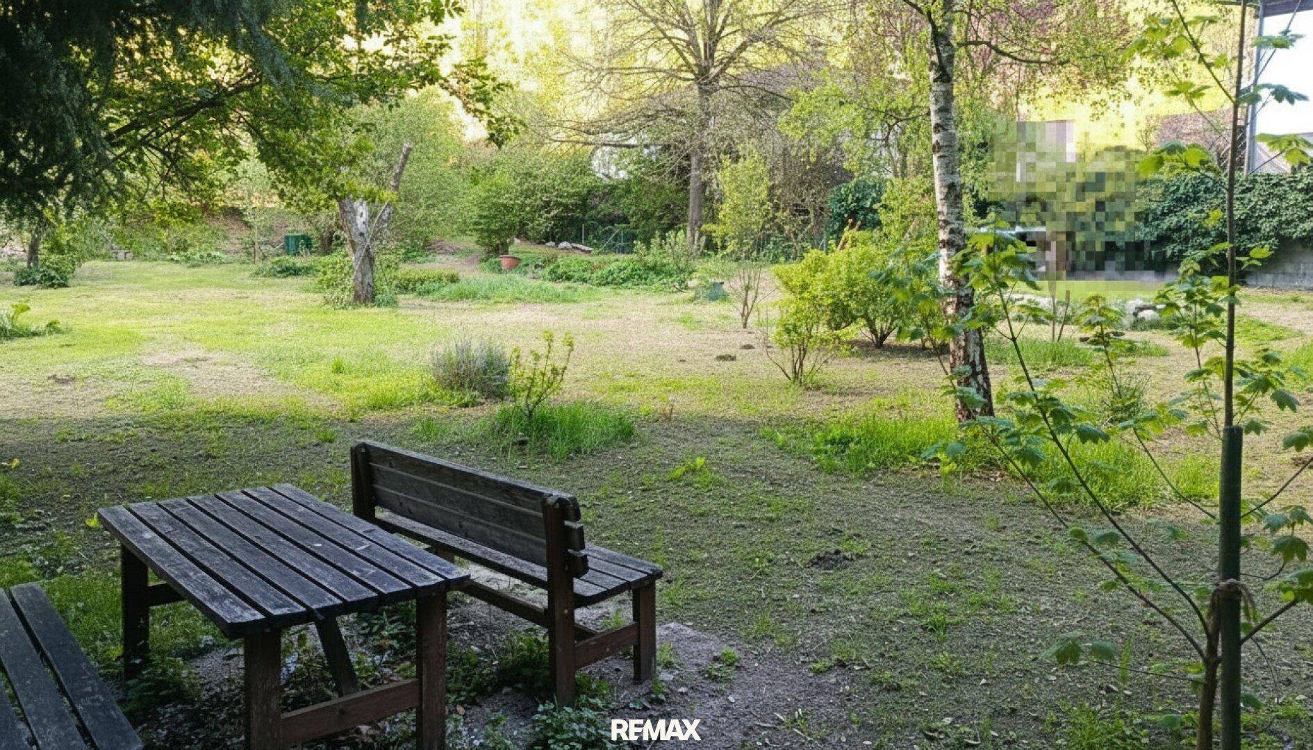 Gemütlicher Gartenbereich mit Holztisch und Bänken, umgeben von Bäumen und Rasenflächen.