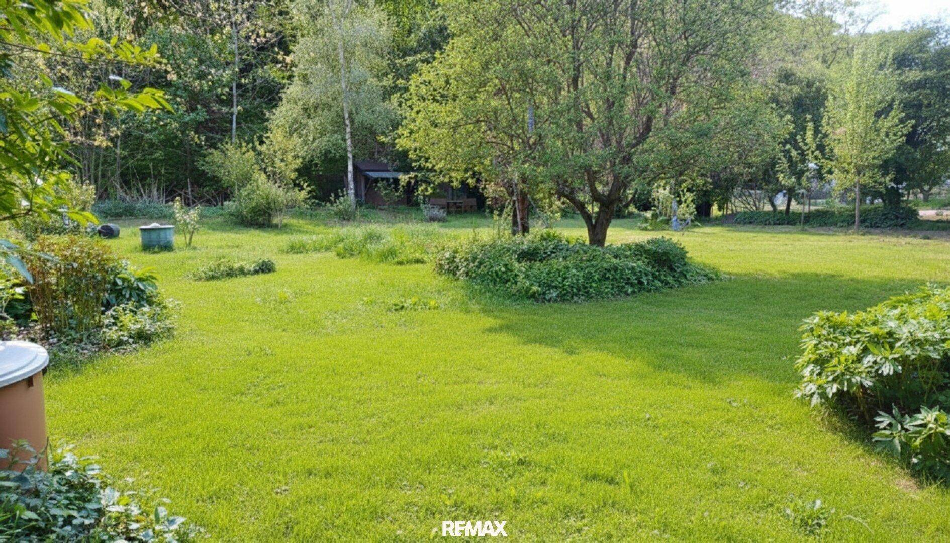 Weitläufiger Gartenbereich mit gepflegtem Rasen und verschiedenen Bäumen und Sträuchern.