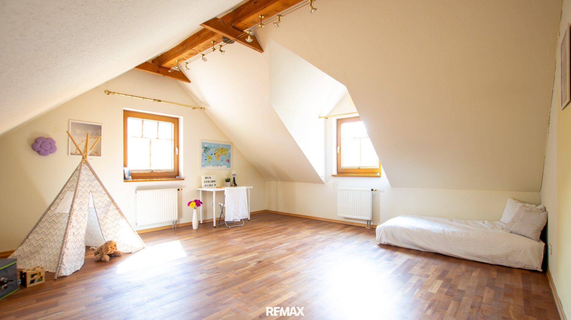 Helles Kinderzimmer im Dachgeschoss mit Holzboden, Schrägen und Spielbereich.