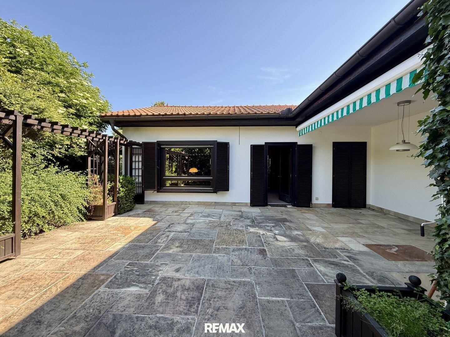 Große gepflasterte Terrasse mit Pergola und Markise, ideal für entspannte Stunden im Freien.
