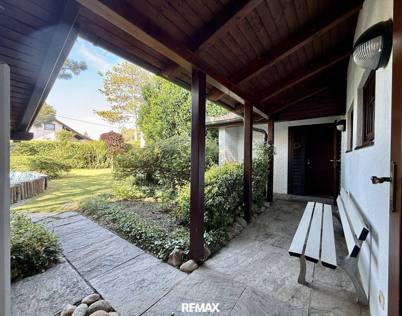 Überdachter Eingangsbereich mit Sitzbank und Blick auf den grünen Garten.
