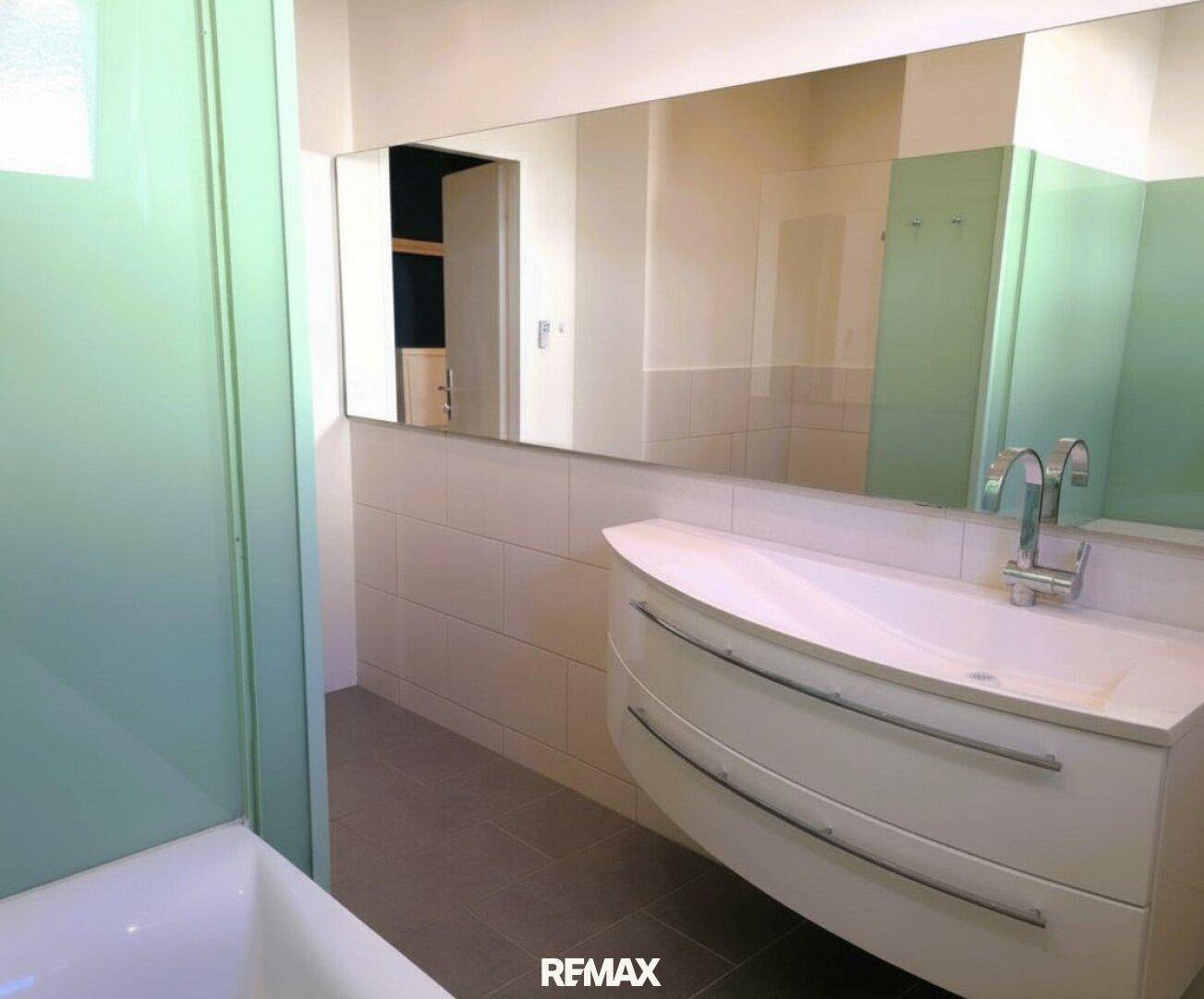 Modernes Badezimmer mit großem Spiegel, elegantem Waschbecken und hellen Fliesen.