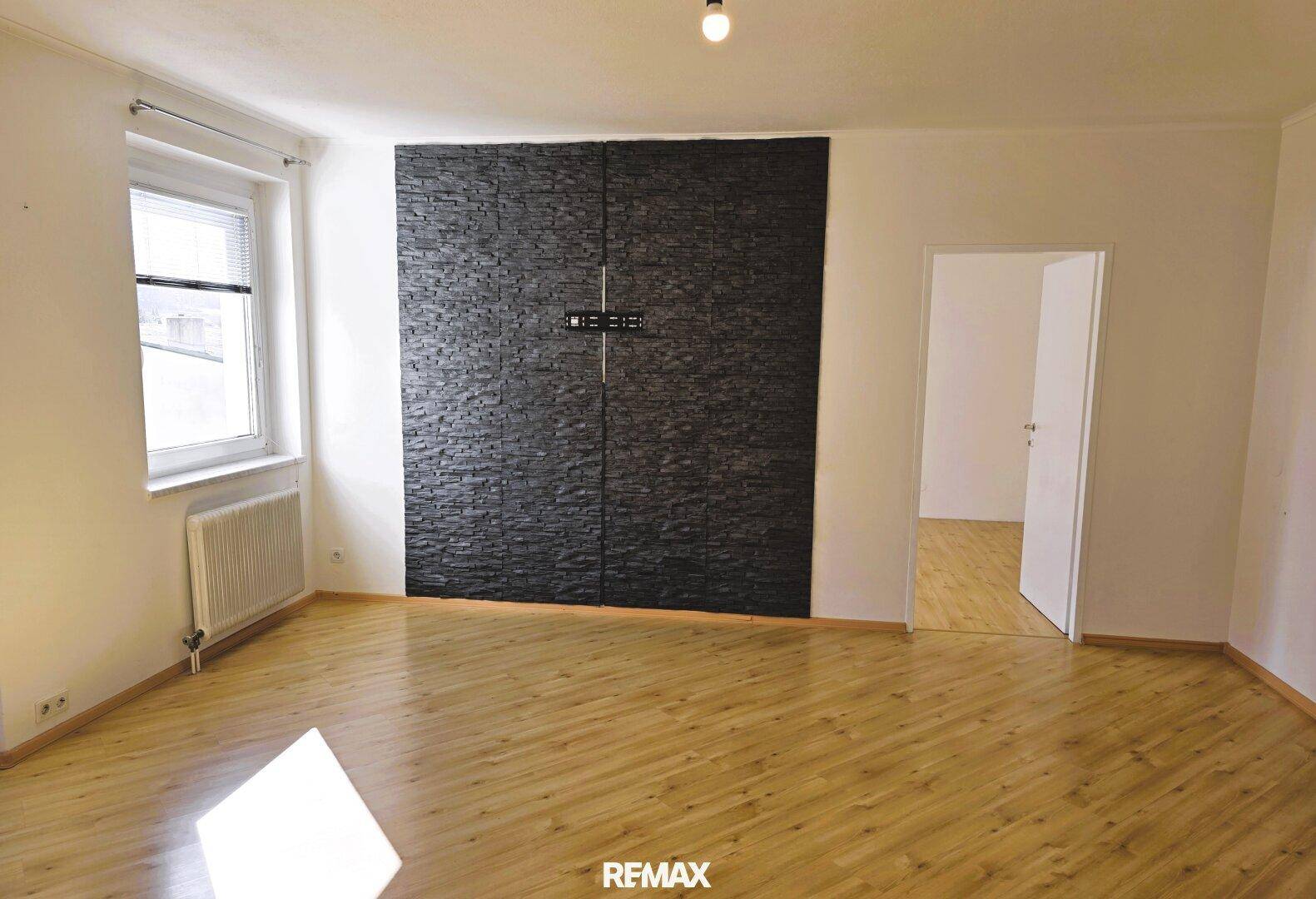 Leeres Wohnzimmer mit hellem Holzboden und einer markanten schwarzen Steinwand.