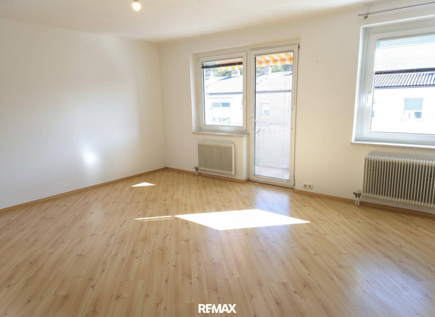 Helles, leeres Wohnzimmer mit Holzboden und direktem Zugang zu einem Balkon.