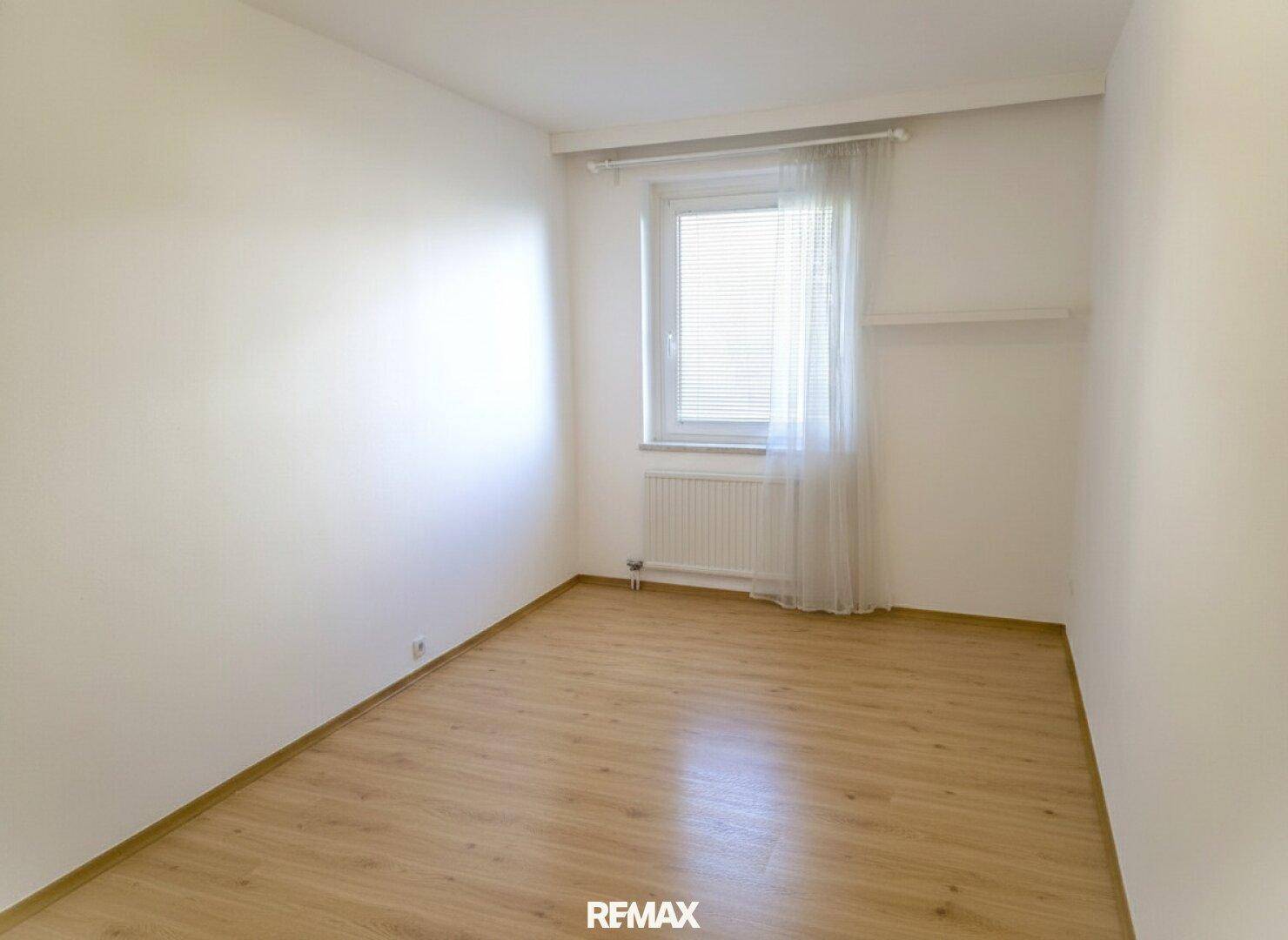 Leeres Zimmer mit hellem Holzboden und Fenster, ideal als Schlaf- oder Arbeitszimmer.