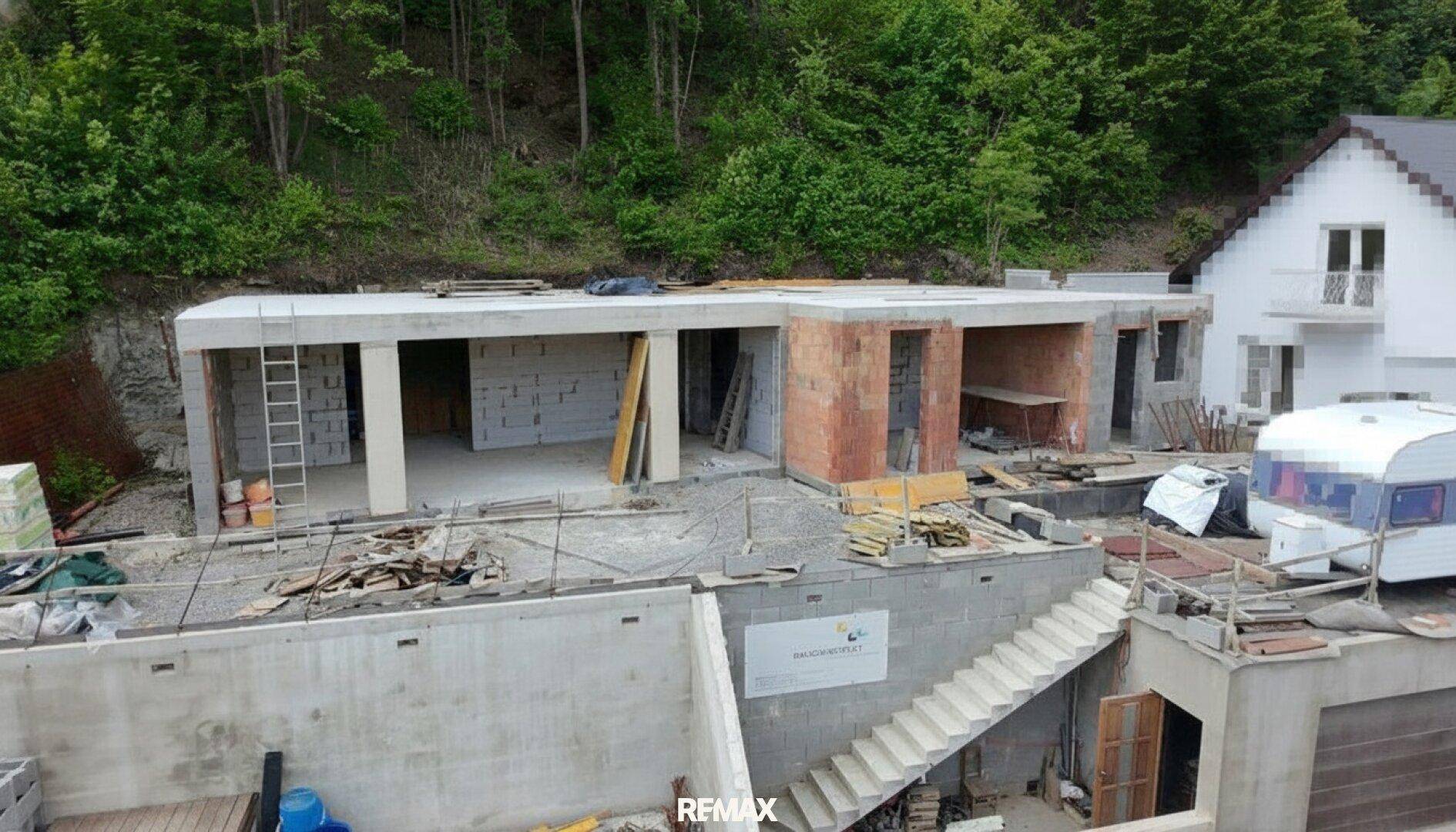 Rohbau eines modernen Gebäudes mit sichtbaren Beton- und Ziegelstrukturen in grüner Umgebung.