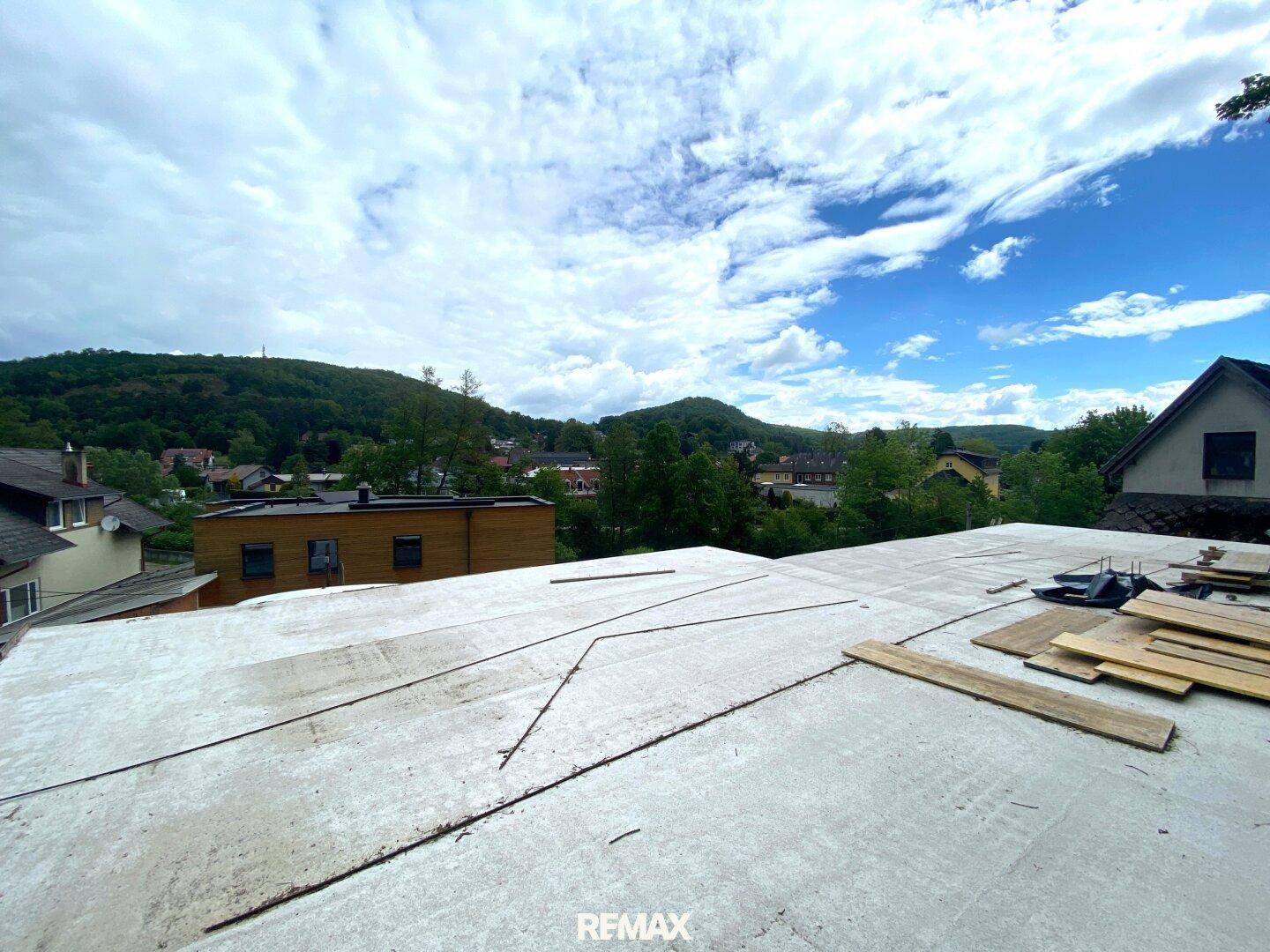Dachfläche im Bau mit Blick auf die hügelige, grüne Landschaft und umliegende Häuser.