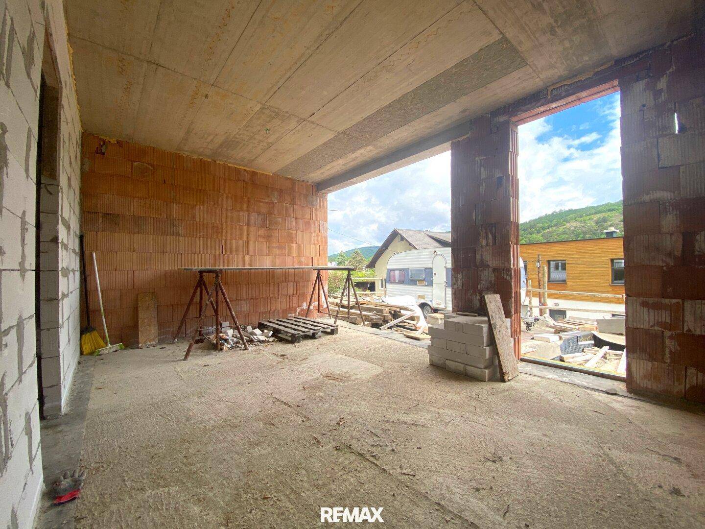 Großer Rohbauraum mit Blick ins Grüne und auf benachbarte Gebäude.