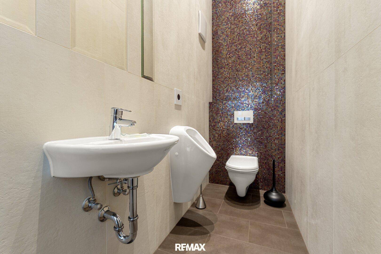 Modernes Gäste-WC mit Urinal, Waschbecken und dekorativer Mosaikwand.