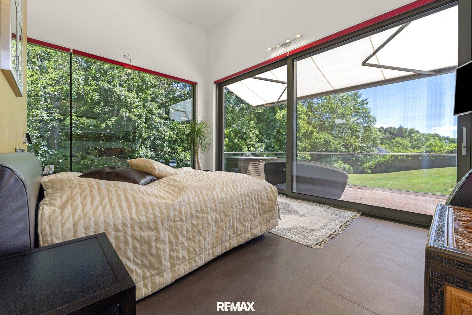 Schlafzimmer mit bodentiefen Fenstern und direktem Zugang zur Terrasse mit Waldblick.