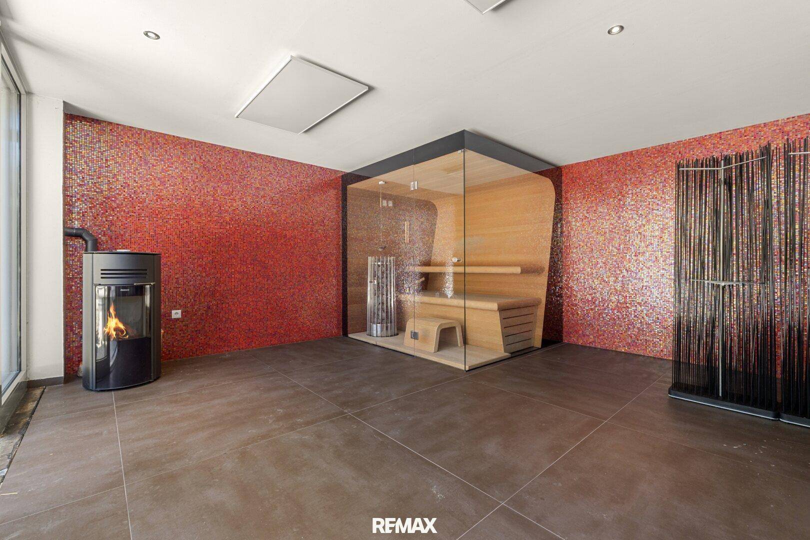 Exklusiver Wellnessbereich mit moderner Sauna, Holzofen und farbenfroher Mosaikwand.