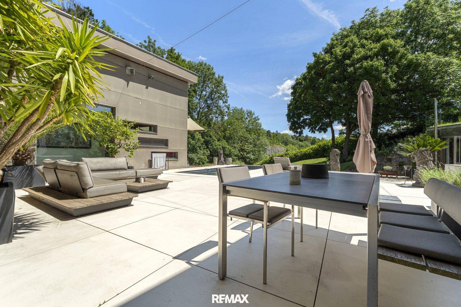 Sonniger Terrassenbereich mit Esstisch, Stühlen und Blick auf den Pool und die Lounge-Möbel.