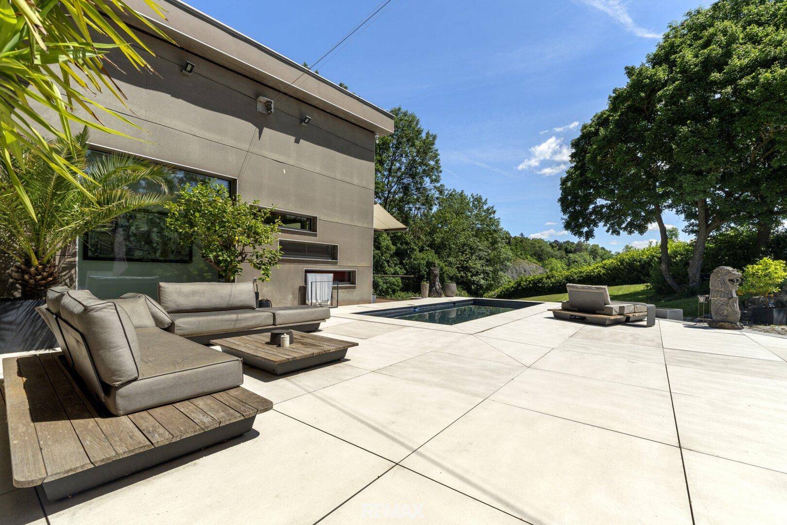 Geräumige Terrasse mit Lounge-Möbeln und einem eleganten Swimmingpool unter blauem Himmel.
