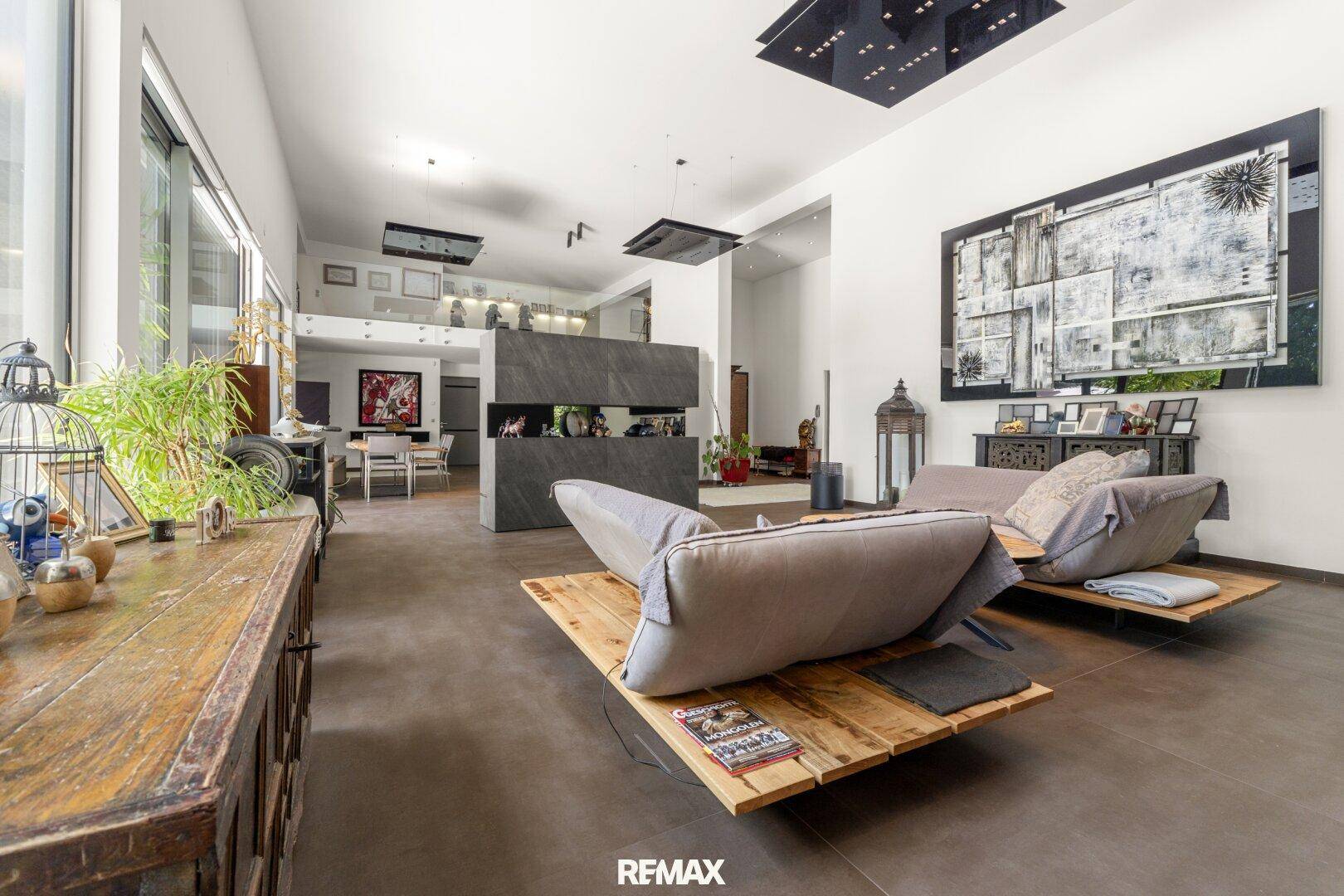 Großzügiges Wohnzimmer mit modernen Liegemöbeln, hohen Decken und großen Fenstern.