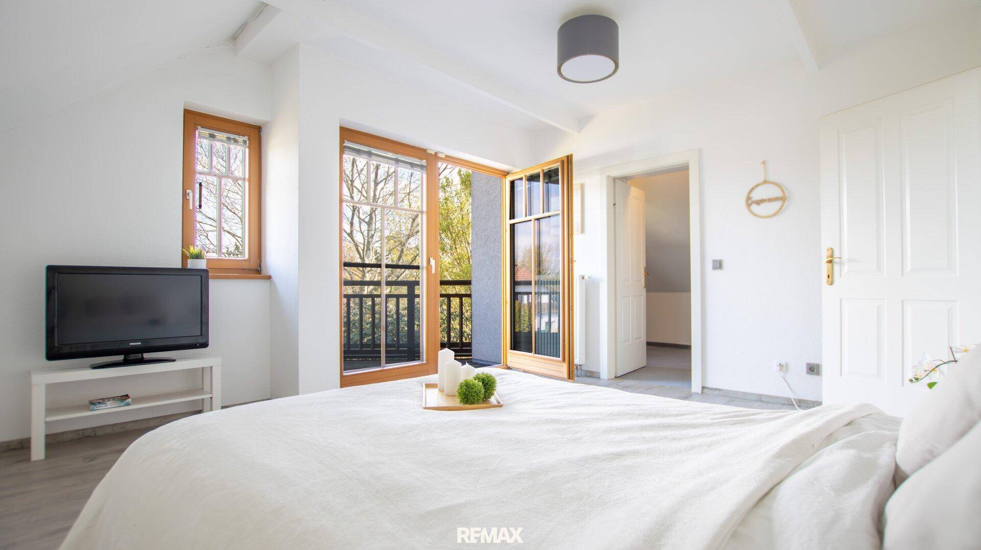Helles Schlafzimmer mit Balkonzugang, Holzboden und Blick ins Grüne.