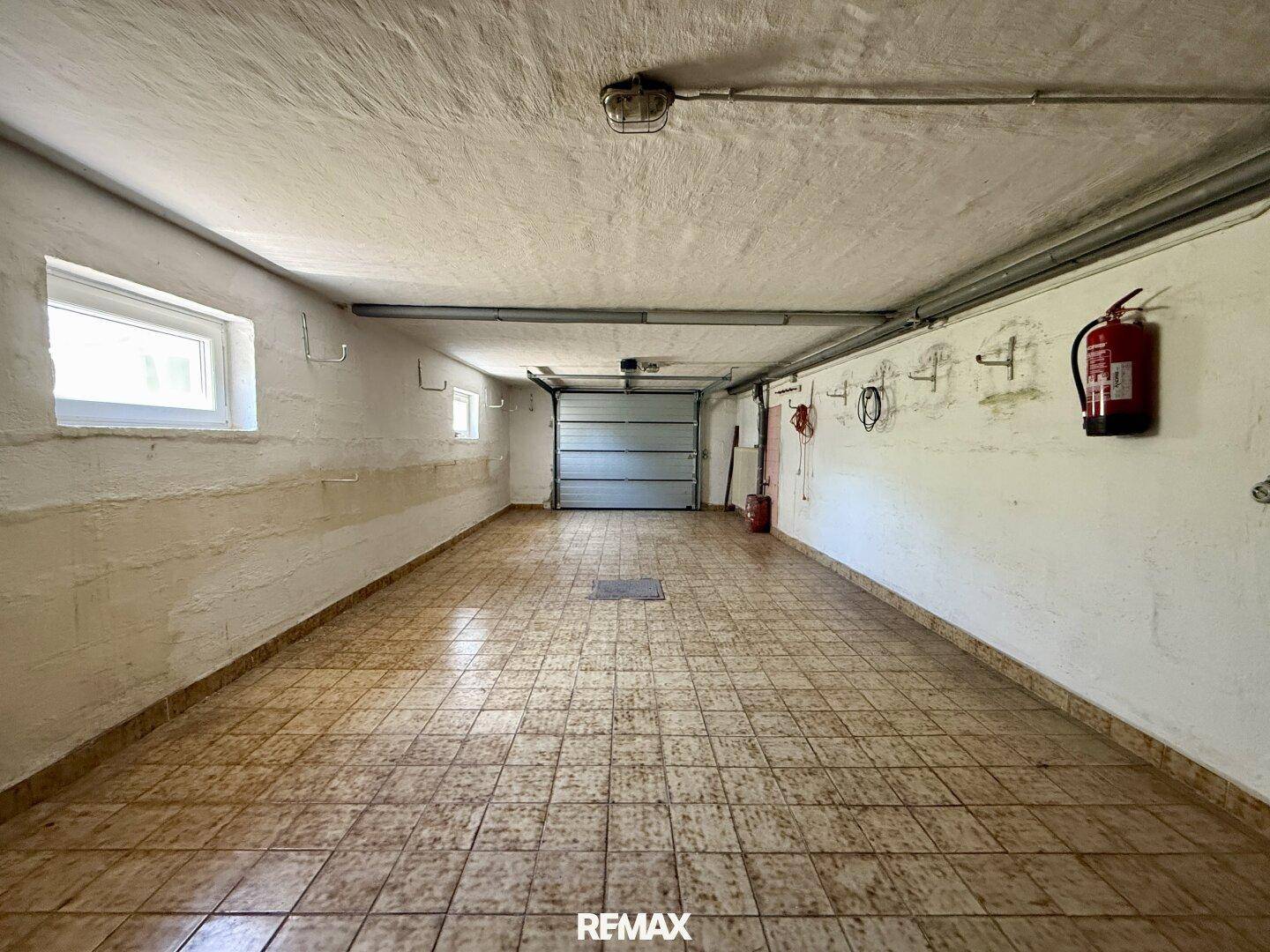 Geräumige Garage mit Fliesenboden, Fenster und Rolltor, bietet viel Platz.