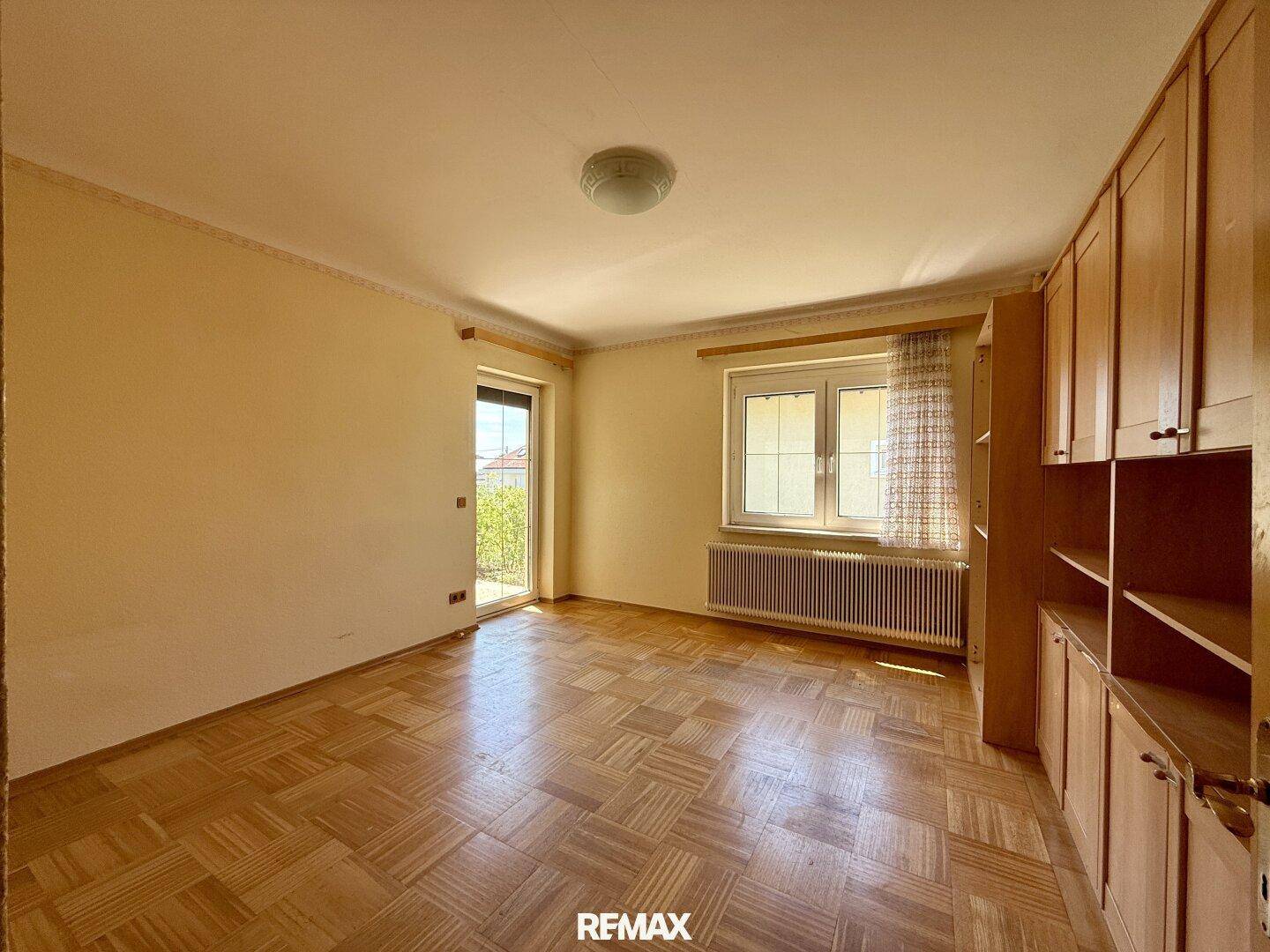 Leeres Schlafzimmer mit Parkettboden, Zugang zum Balkon und Einbauschränken.
