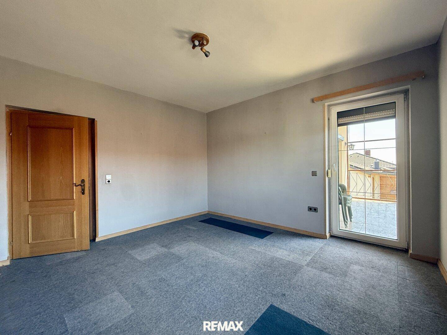 Leeres Zimmer mit Teppichboden und Zugang zu einem Balkon, ideal als Schlafzimmer.
