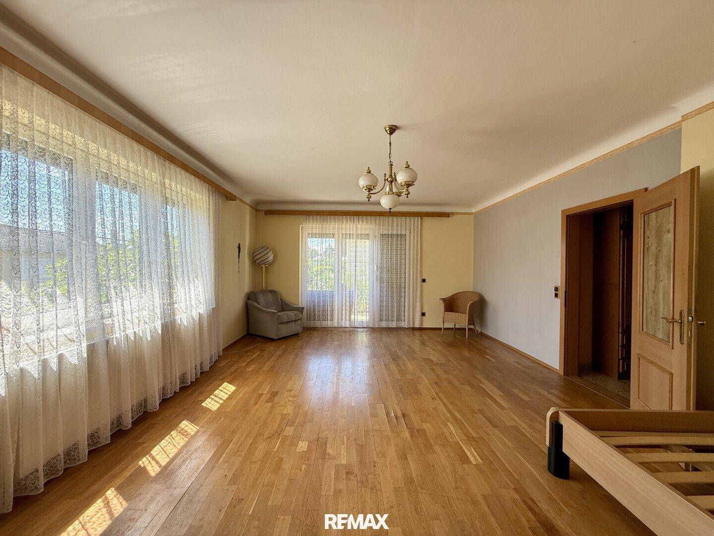 Helles Wohnzimmer mit Parkettboden, großen Fenstern und Zugang zu einem Außenbereich.